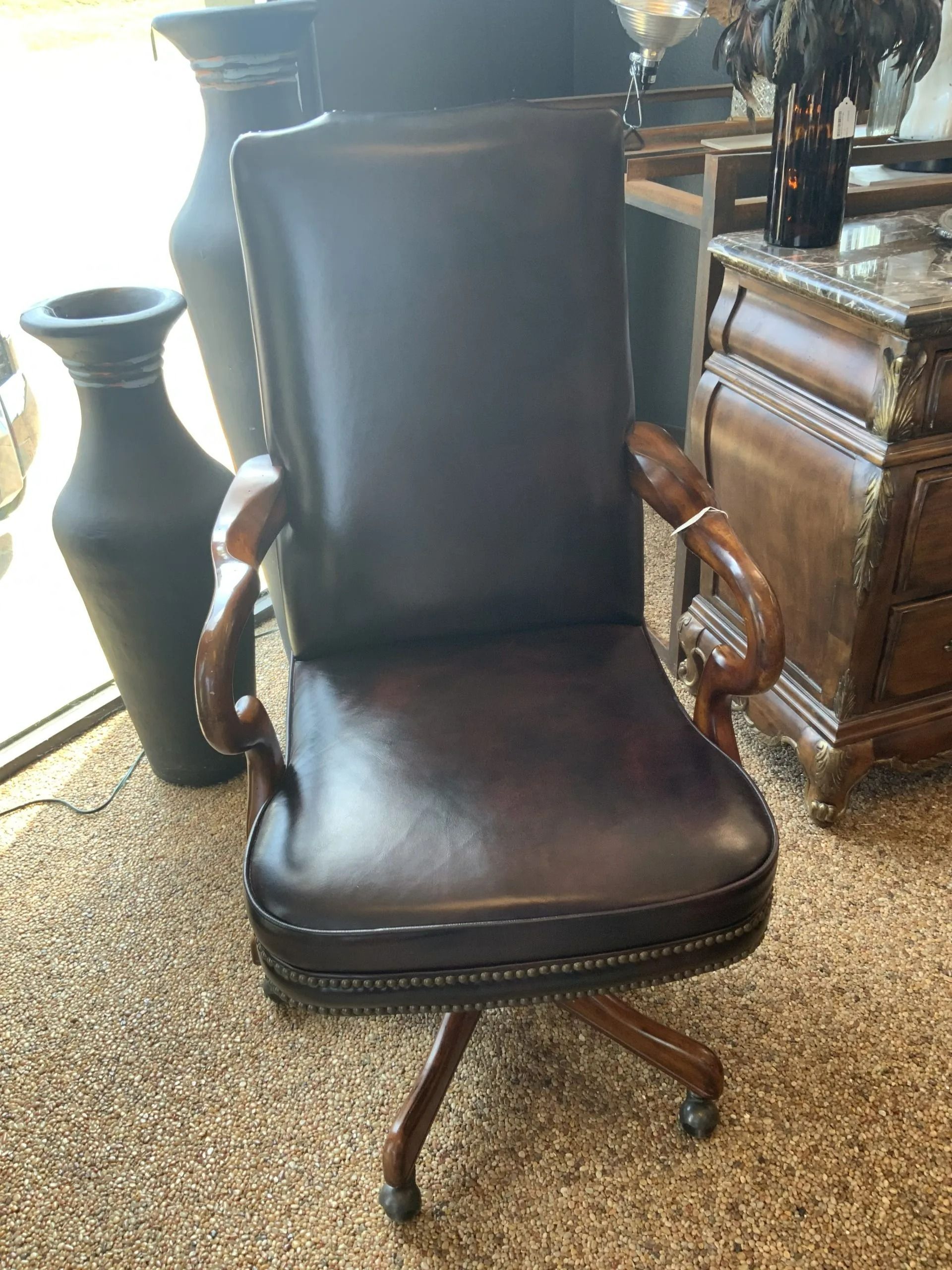 A dark brown leather executive office chair with wooden armrests, positioned on a tan carpet in a showroom.