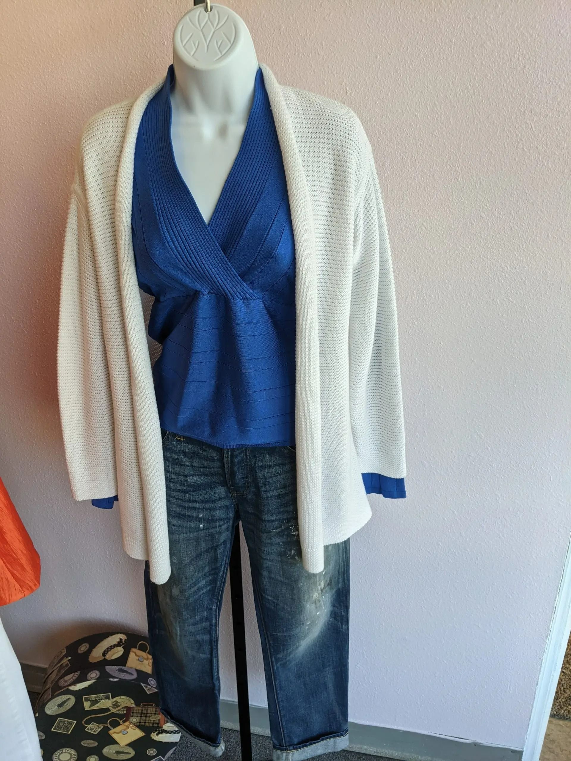 A mannequin displays a blue v-neck sweater, a white open-front knit cardigan, and blue denim jeans.