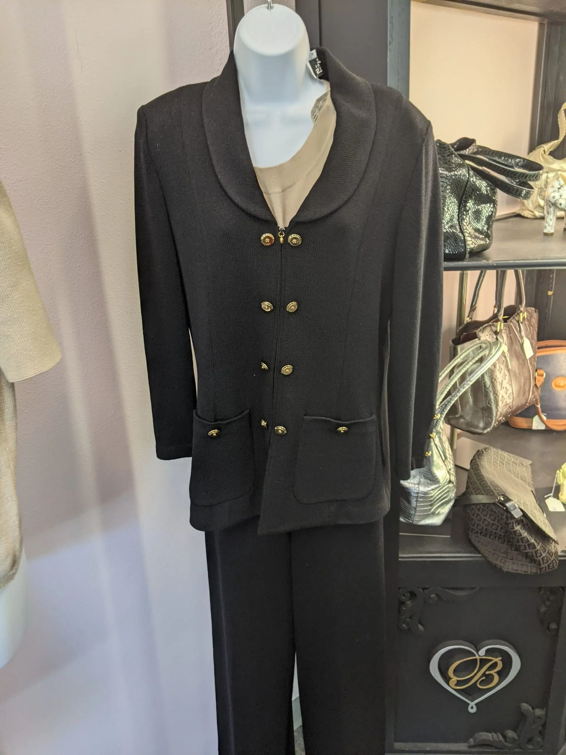 A black knit cardigan with gold buttons and a shawl collar displayed on a mannequin in a shop.