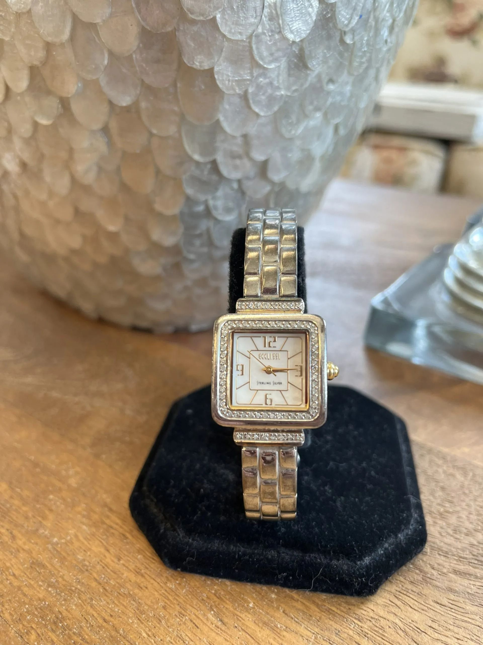A silver-tone square-faced wristwatch with a link bracelet sits upright on a small, black velvet display stand.