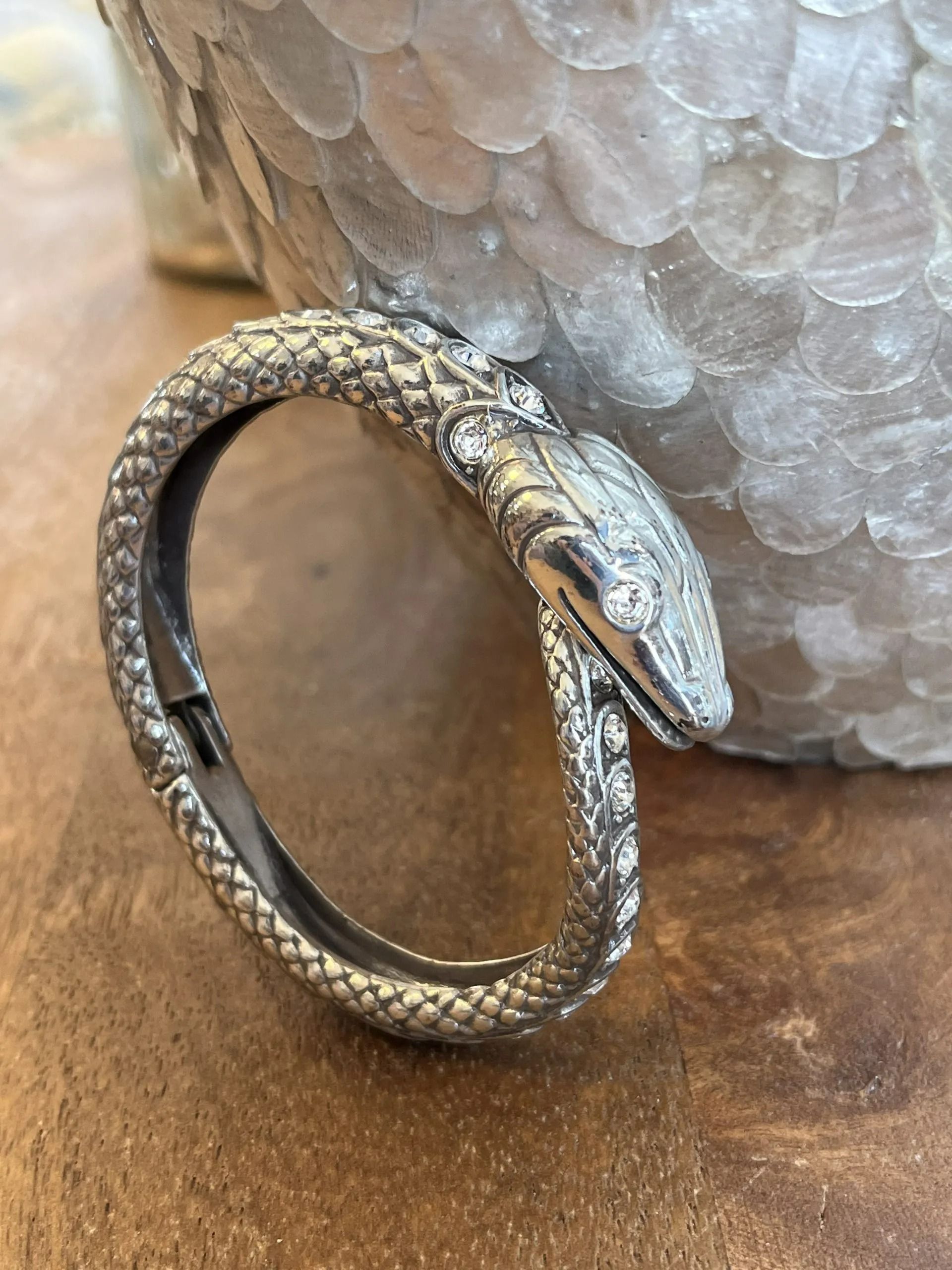 A silver, snake-shaped hinged bracelet with sparkling stone inlays, resting against a textured, metallic object.