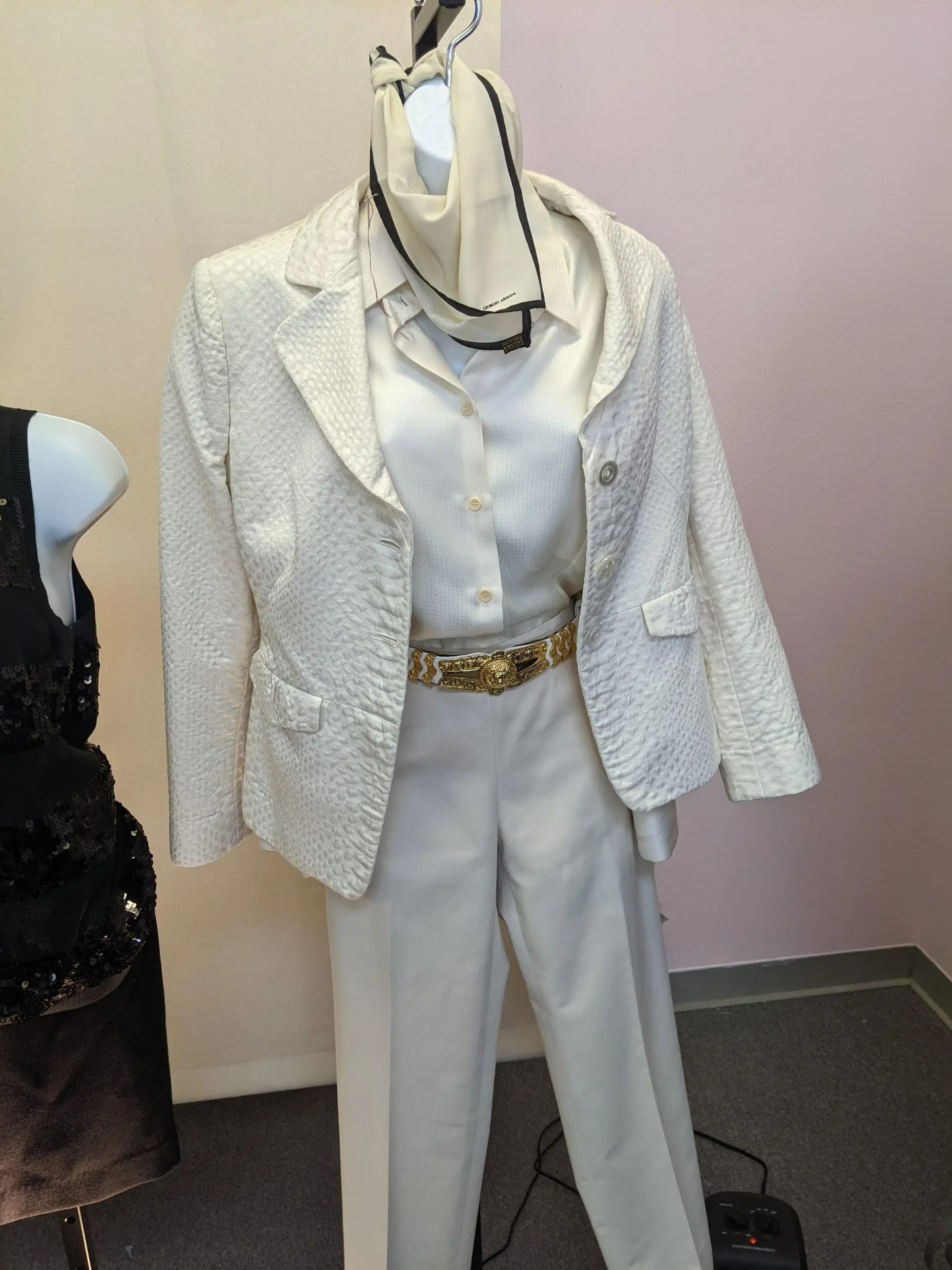 A white textured blazer, button-down shirt, and dress slacks with a gold belt and scarf displayed on a mannequin.