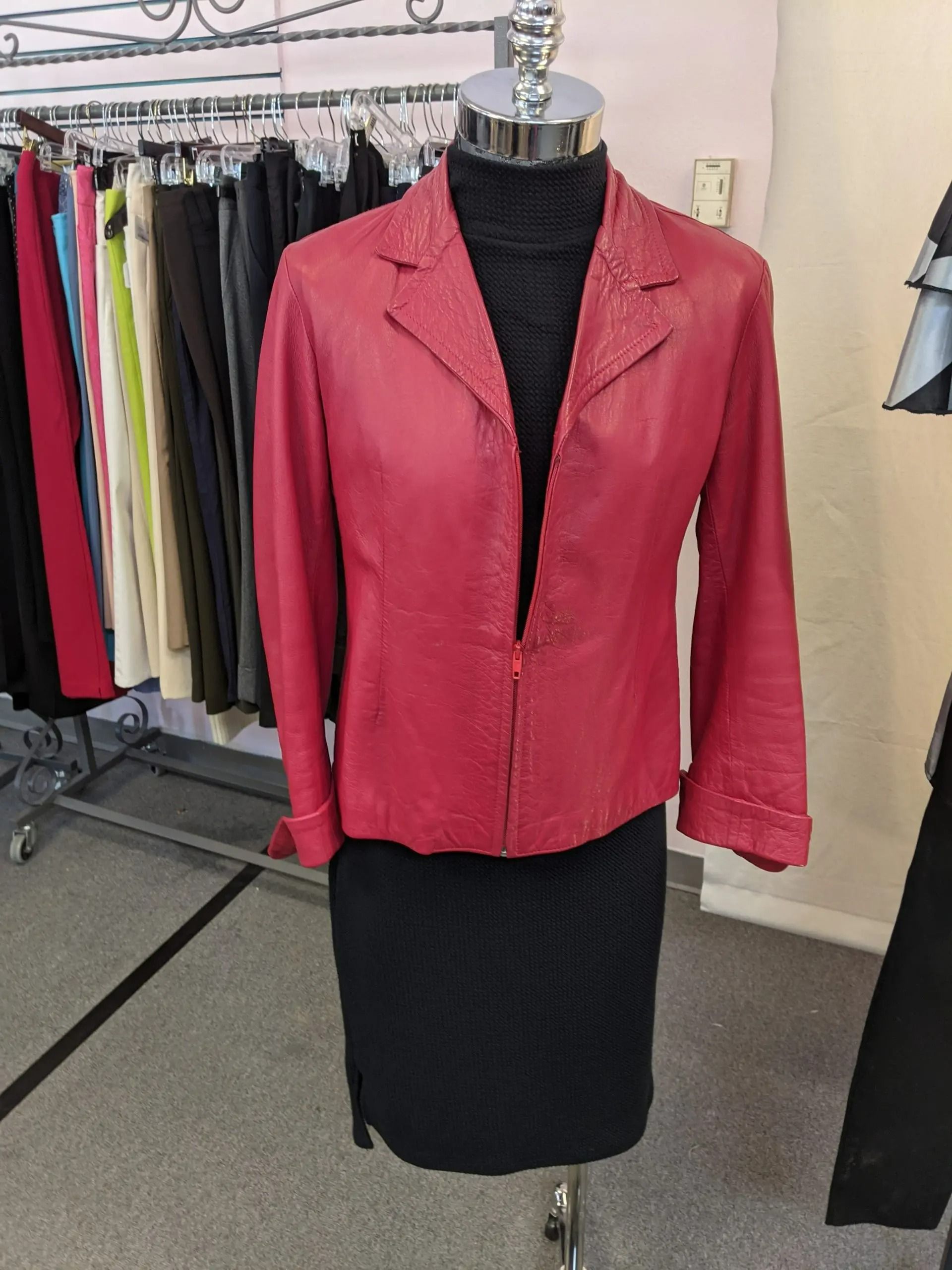 A red leather blazer worn over a black turtleneck and skirt on a mannequin in a clothing store.