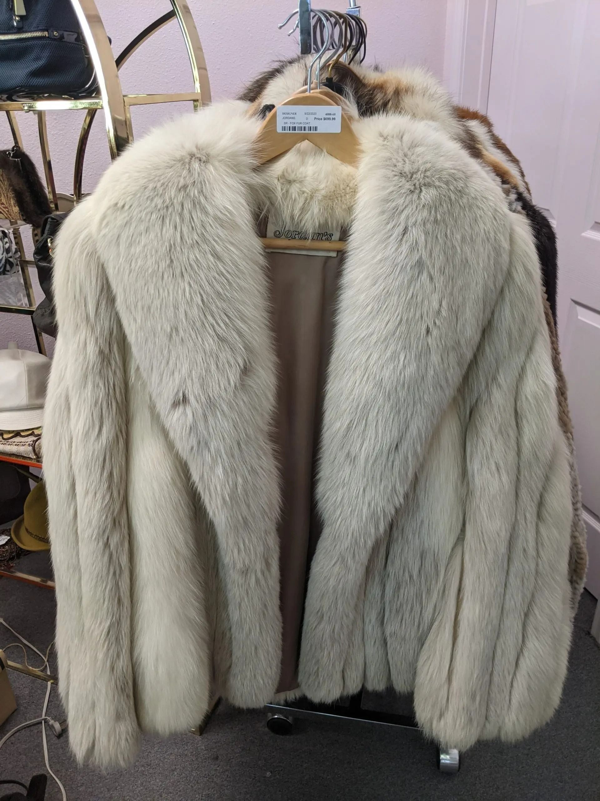 A beige, cream-colored fur coat hangs on a wooden hanger in a retail store setting.