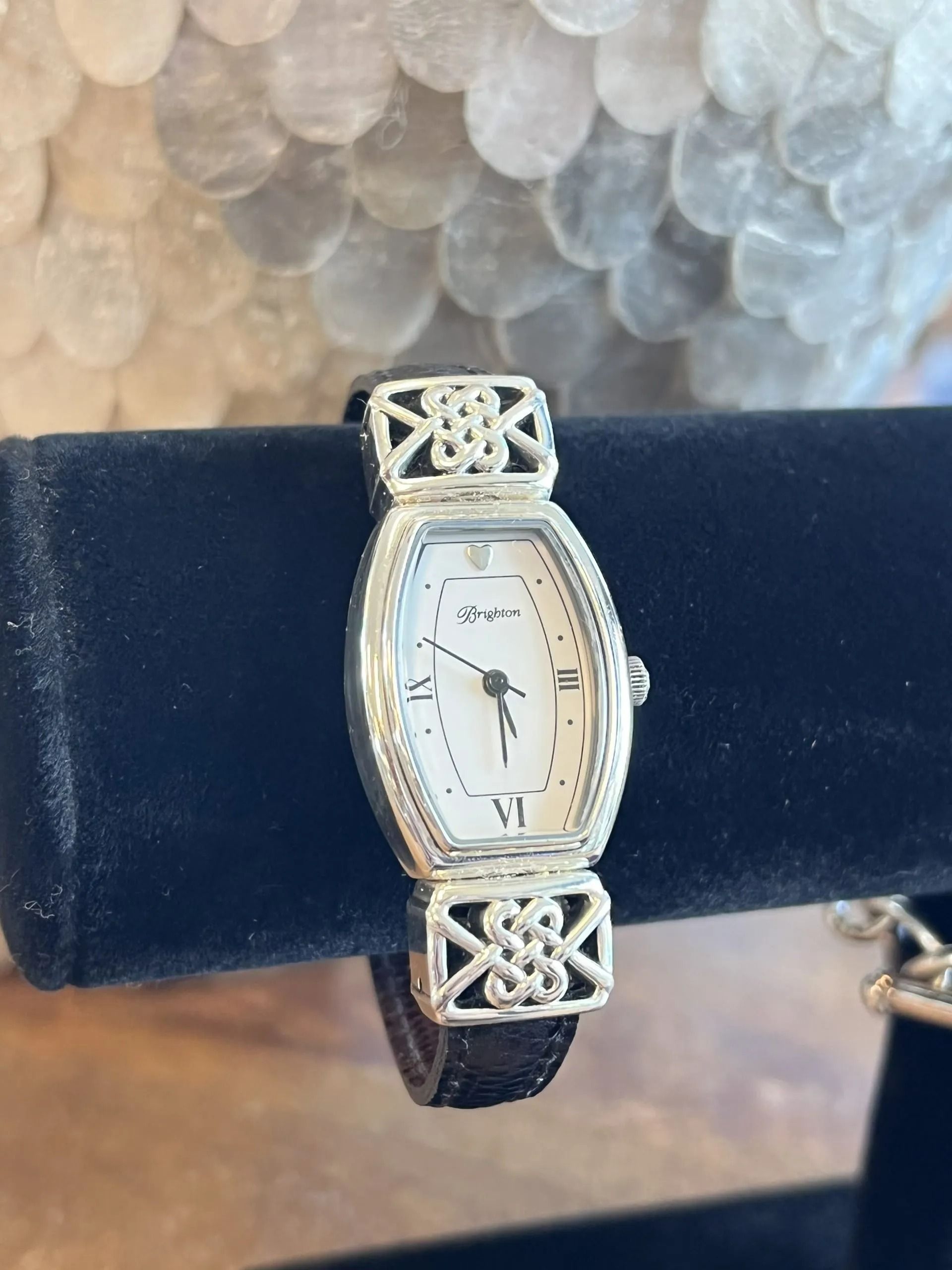 A silver-tone watch with a rectangular white face and intricate Celtic knot links on a dark leather strap.