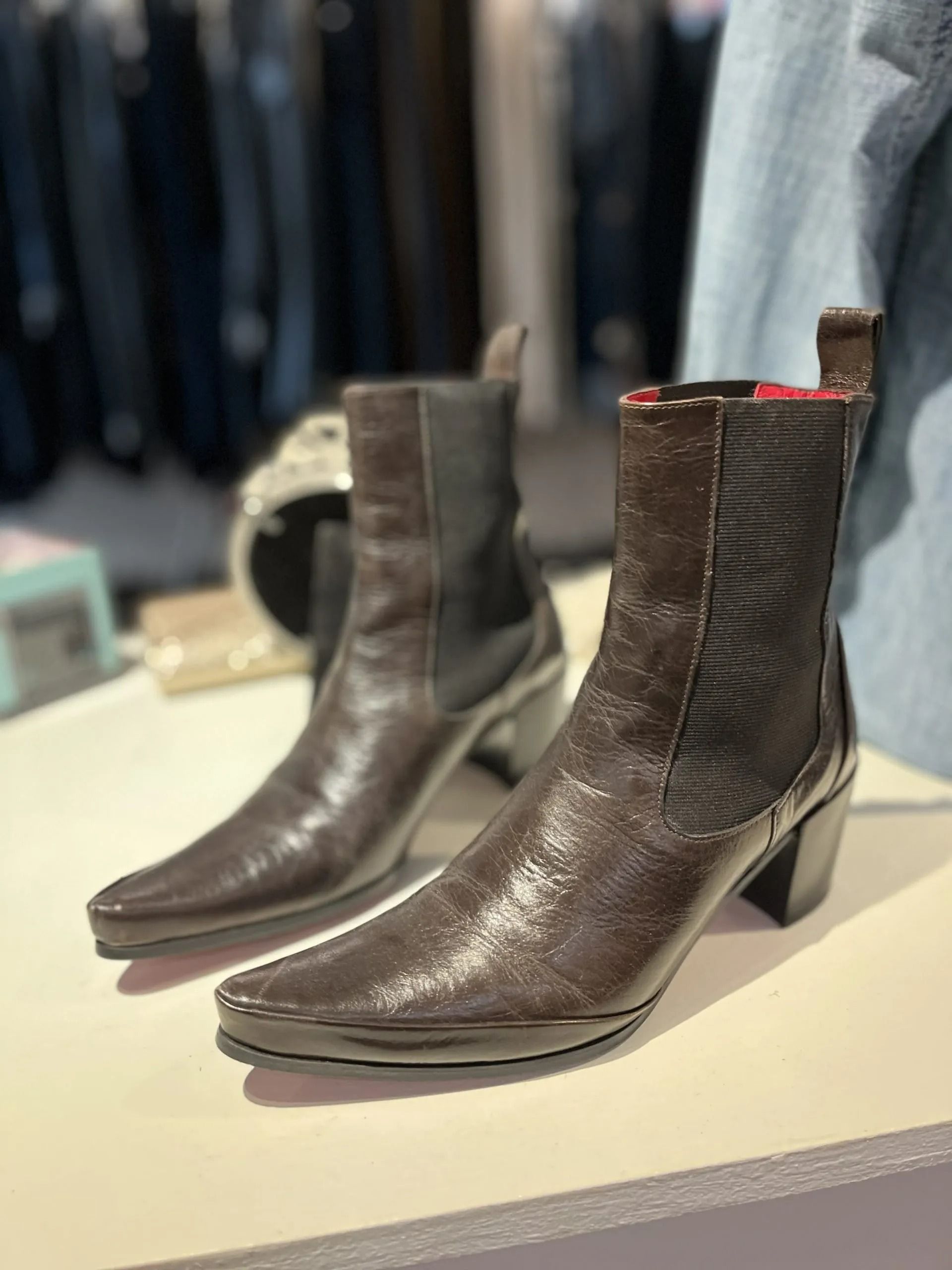 A pair of brown, pointed-toe leather ankle boots with elastic side panels and block heels displayed on a store shelf.