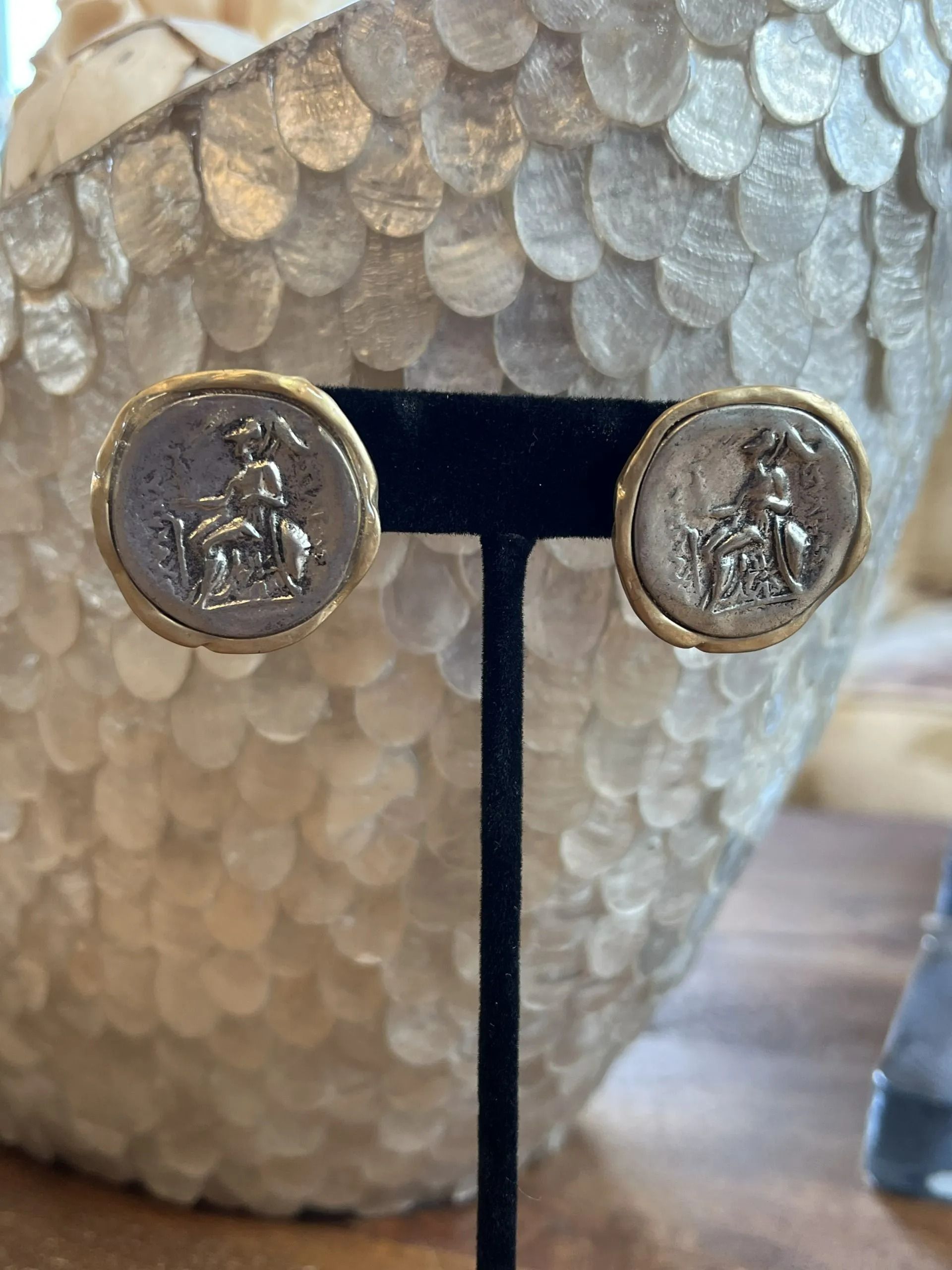 Gold-rimmed clip-on earrings featuring a silver, coin-like design with a relief of a figure on horseback.