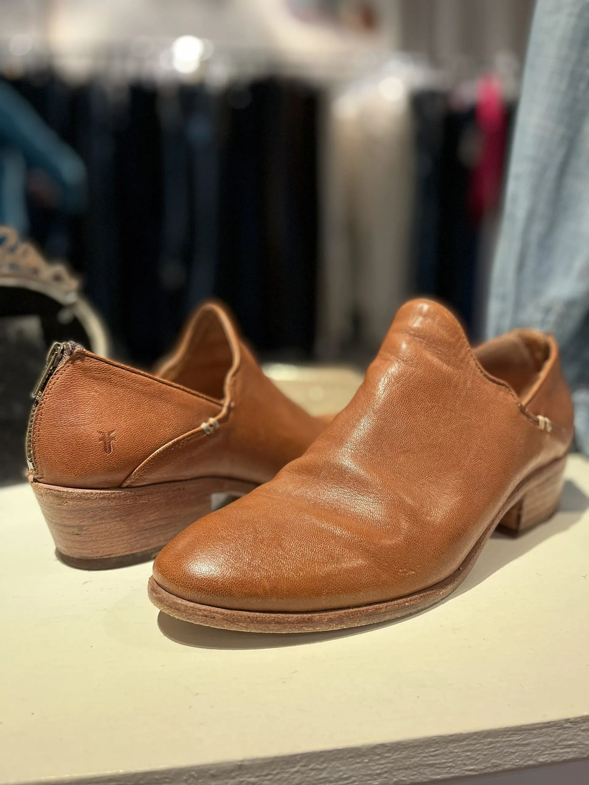 Two tan leather slip-on shoes with textured finishes and low heels displayed on a store counter.