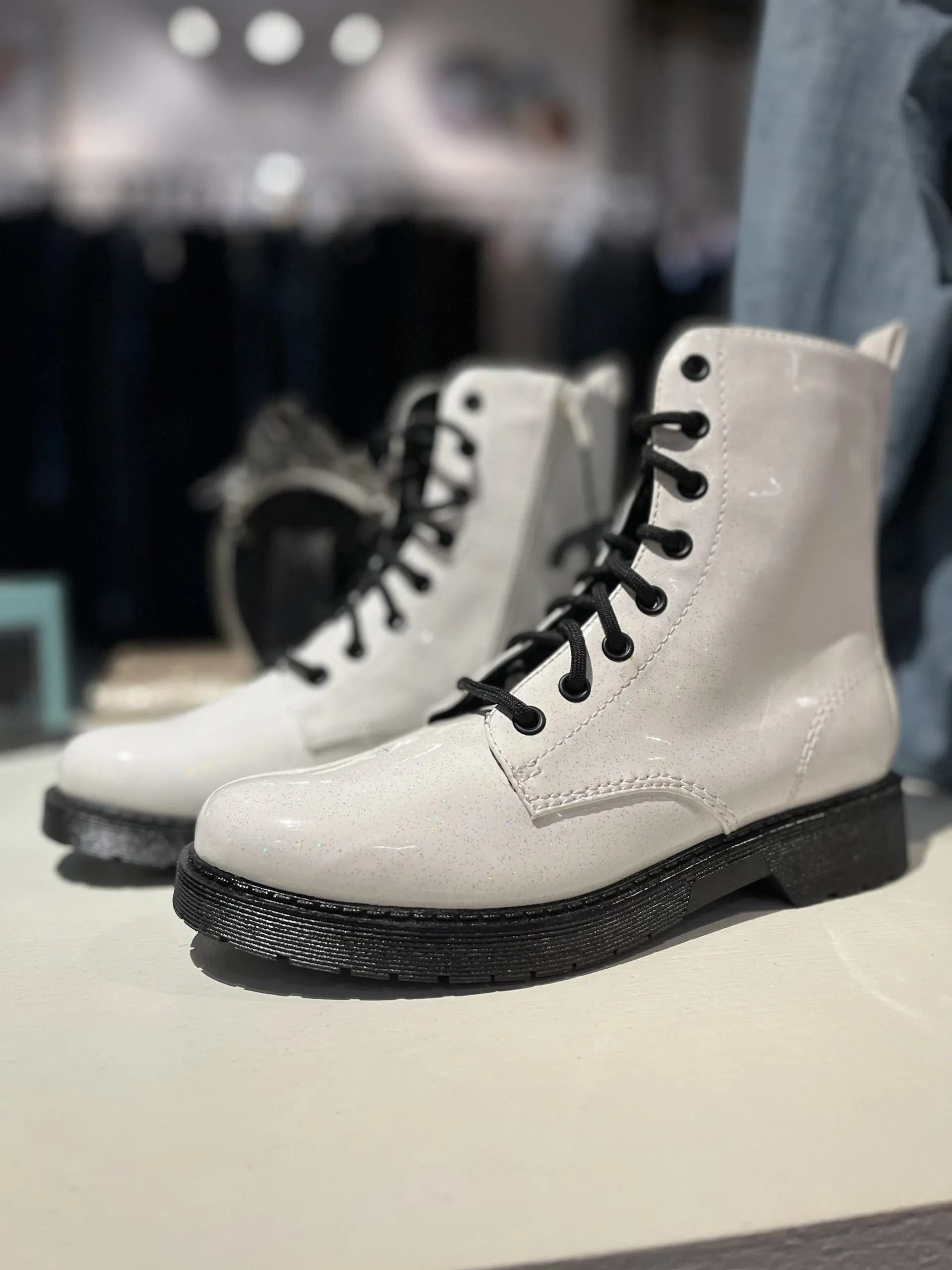 A pair of white, lace-up ankle boots with thick, black textured soles, displayed on a shelf in a store.