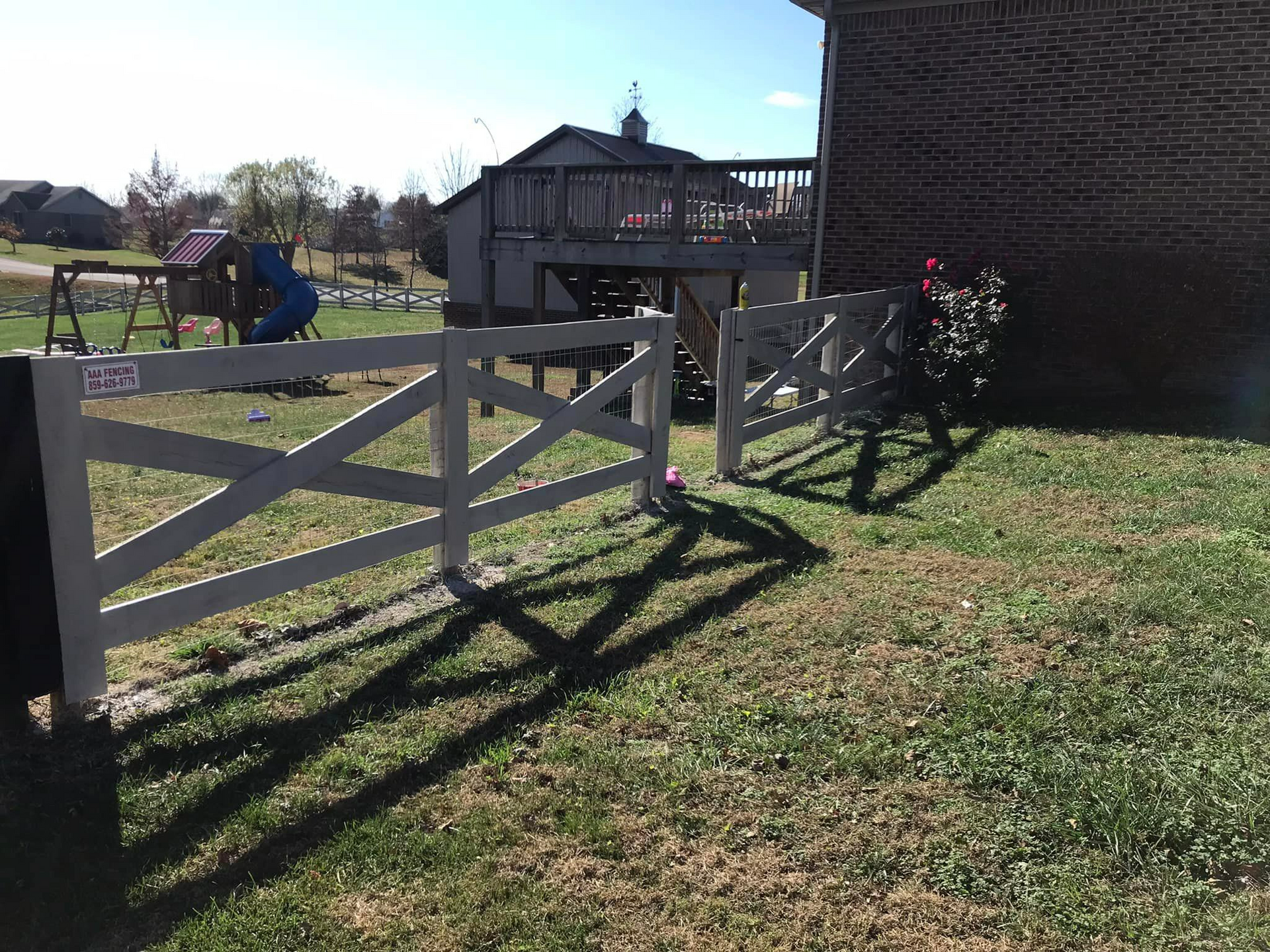 A white fence surrounds a lush green yard in front of a house.