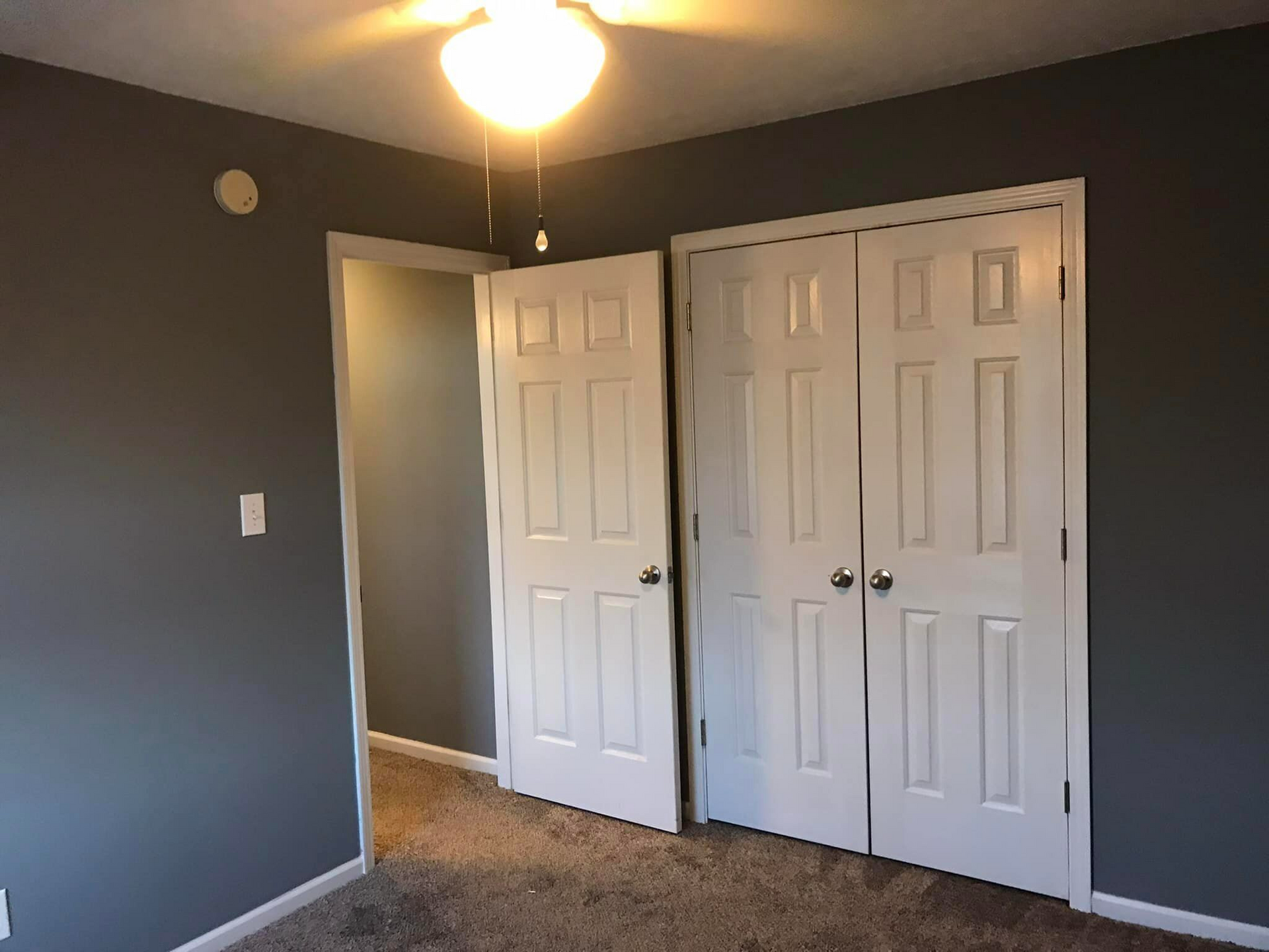 An empty bedroom with two closets and a ceiling fan.