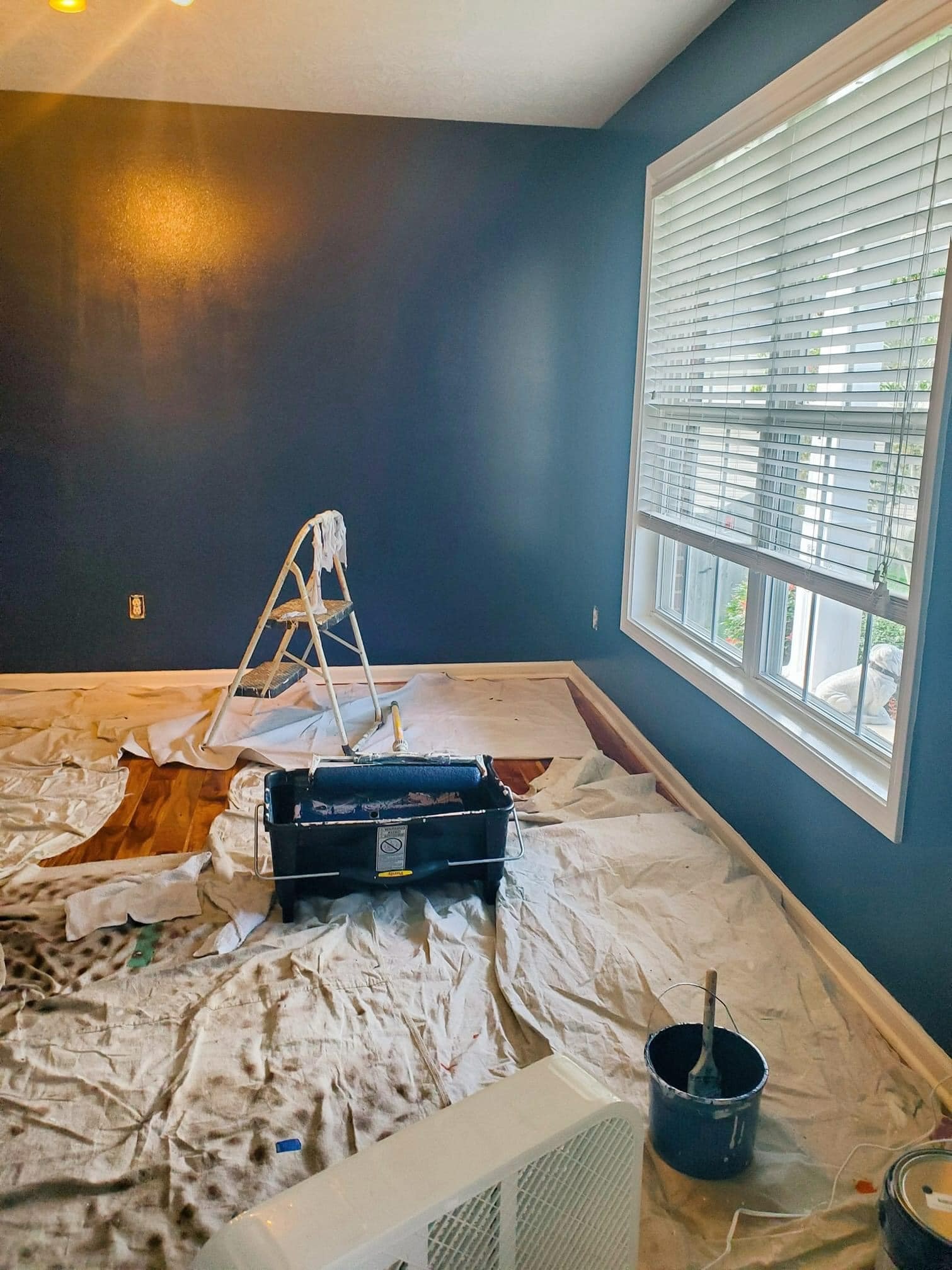 A room is being painted with blue walls and white blinds.