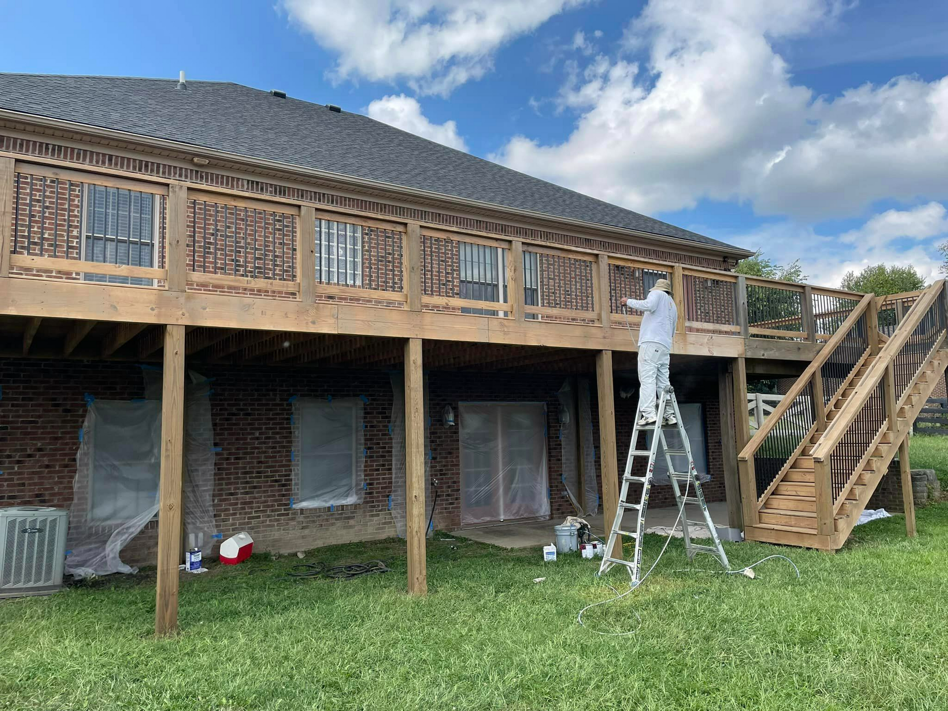 A man is standing on a ladder painting the deck of a house.