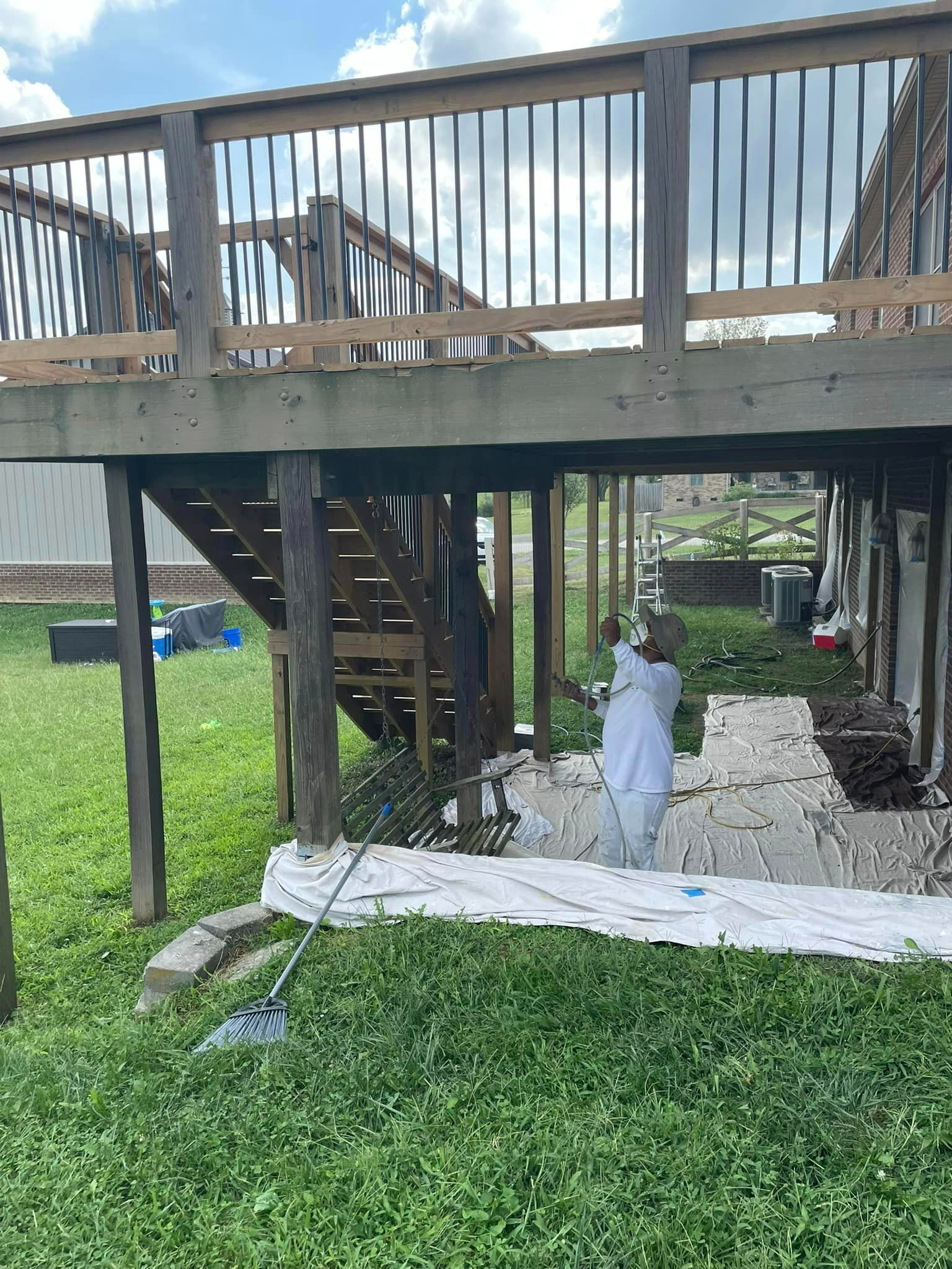 A man is painting a wooden deck in a backyard.