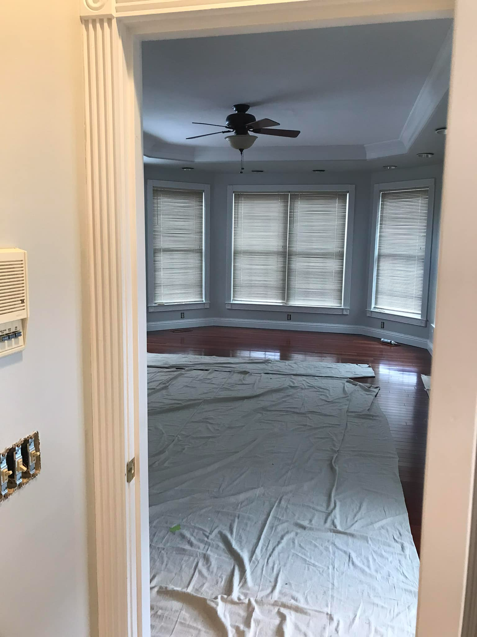 A room with a ceiling fan and a white sheet on the floor.