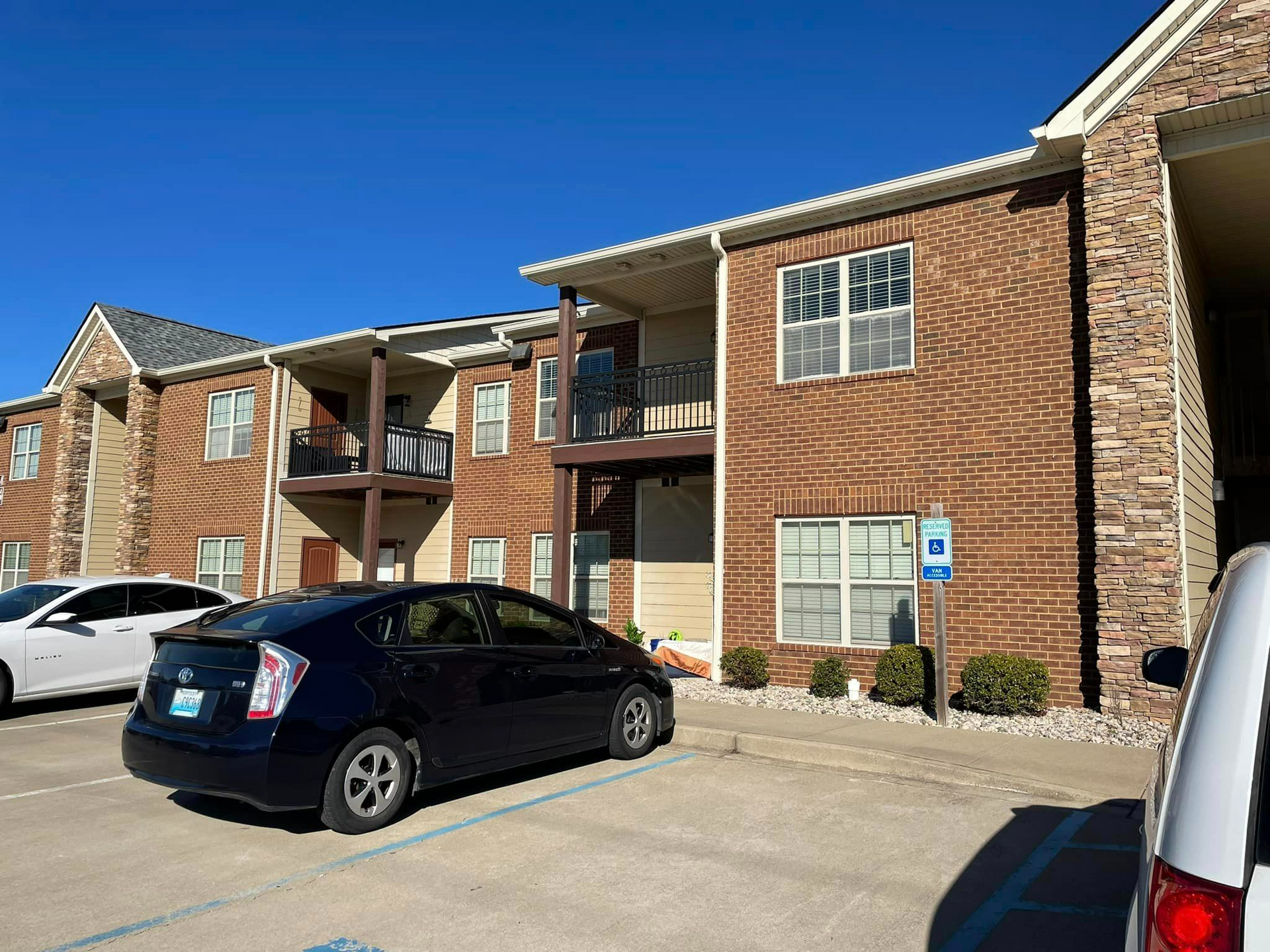 A black car is parked in front of a brick apartment building.