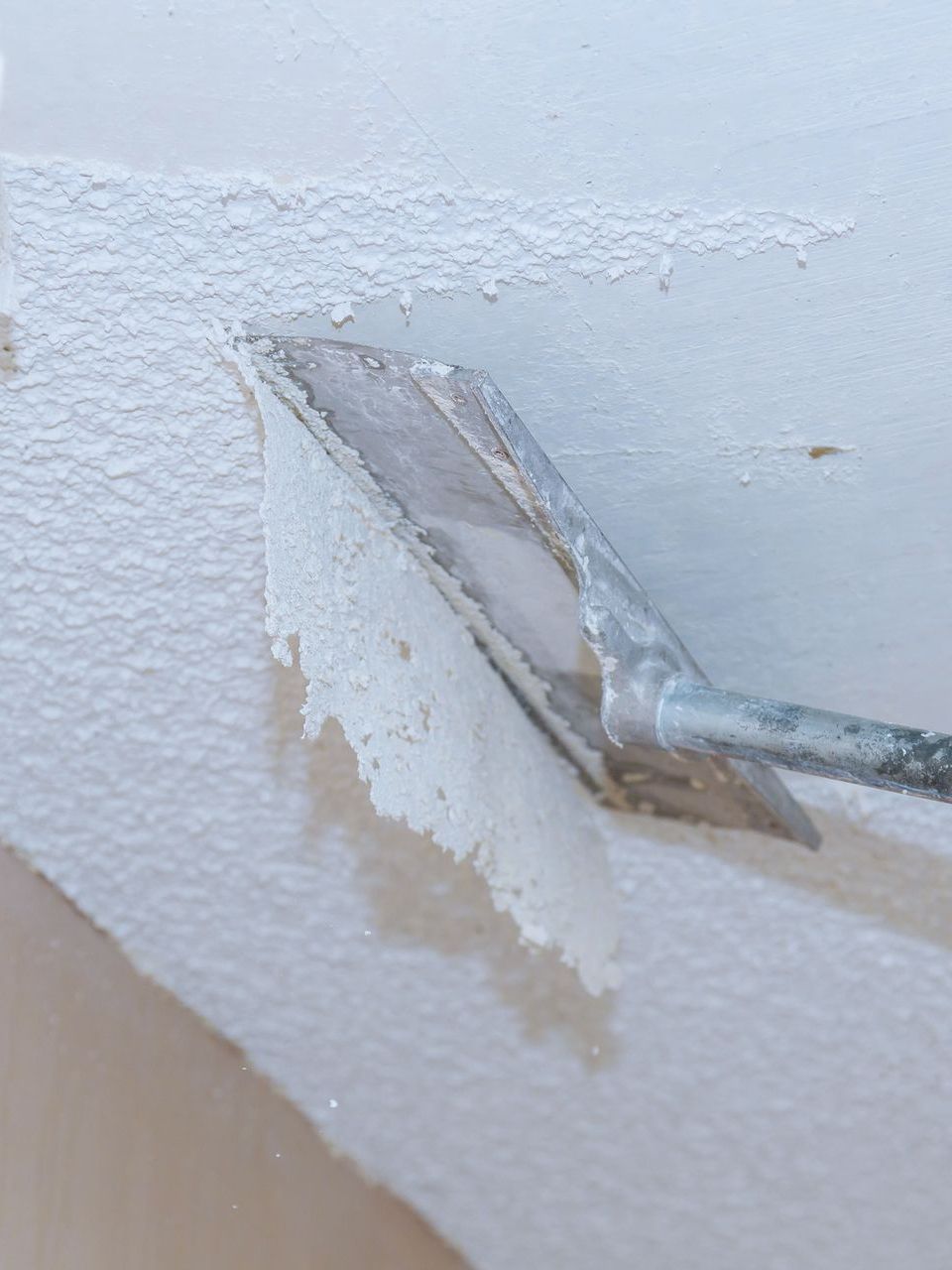 A person is removing wallpaper from a ceiling with a spatula.