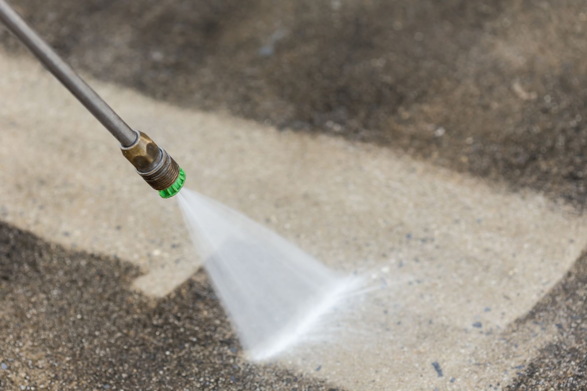 A yellow high pressure washer is spraying water on a brick sidewalk