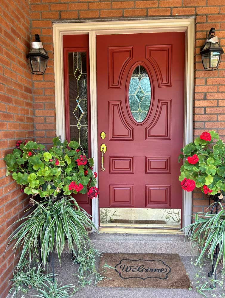 A red door with a welcome mat and potted plants in front of it.