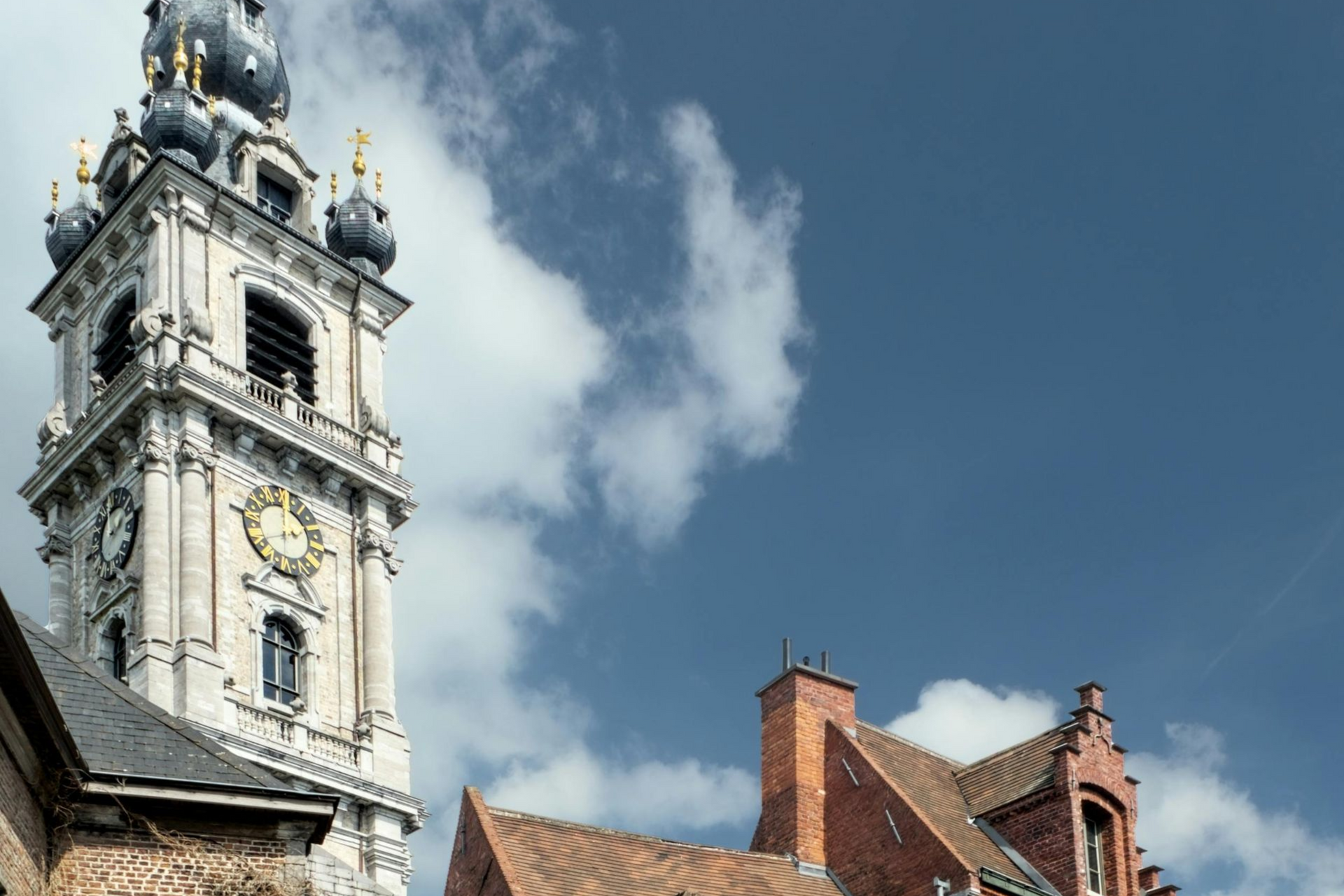 Tour de l'horloge et bâtiments aux toits rouges se détachant sur un ciel bleu parsemé de nuages