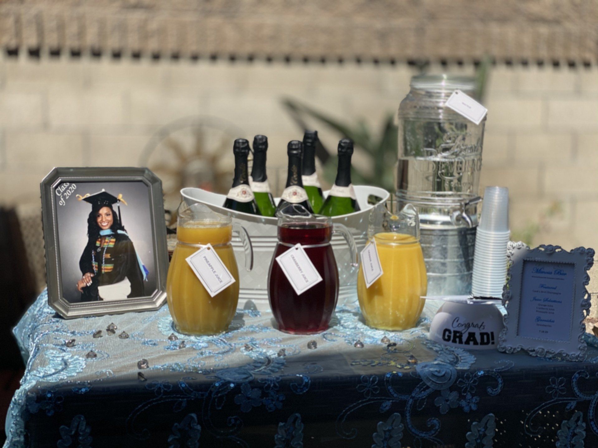 Graduation celebration table with beverages: juice, water, champagne, and a framed photo.