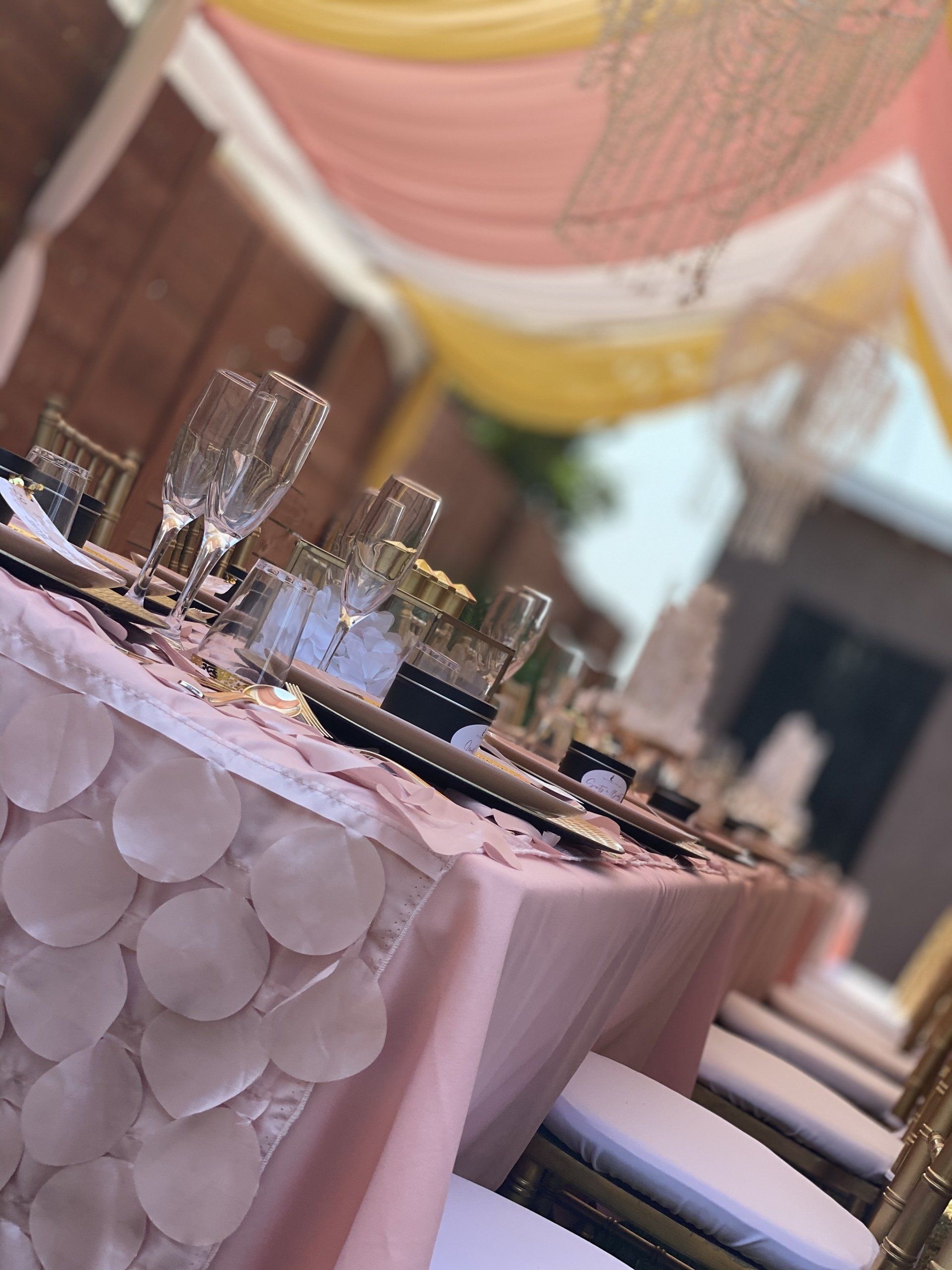 Long table set for a celebration, pink and gold decor. Champagne flutes, plates, and a cake.
