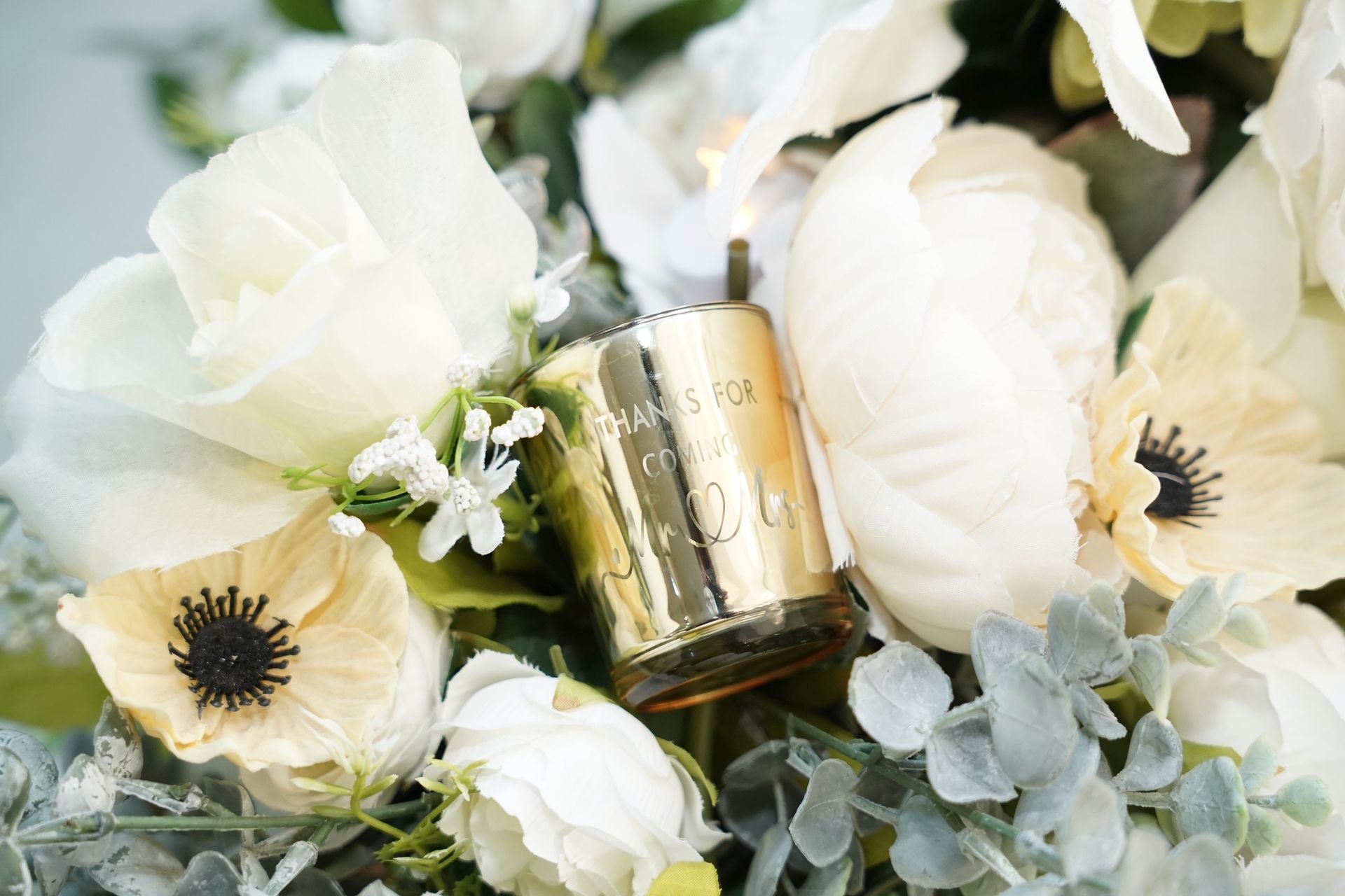 Golden candle nestled among white flowers and greenery.
