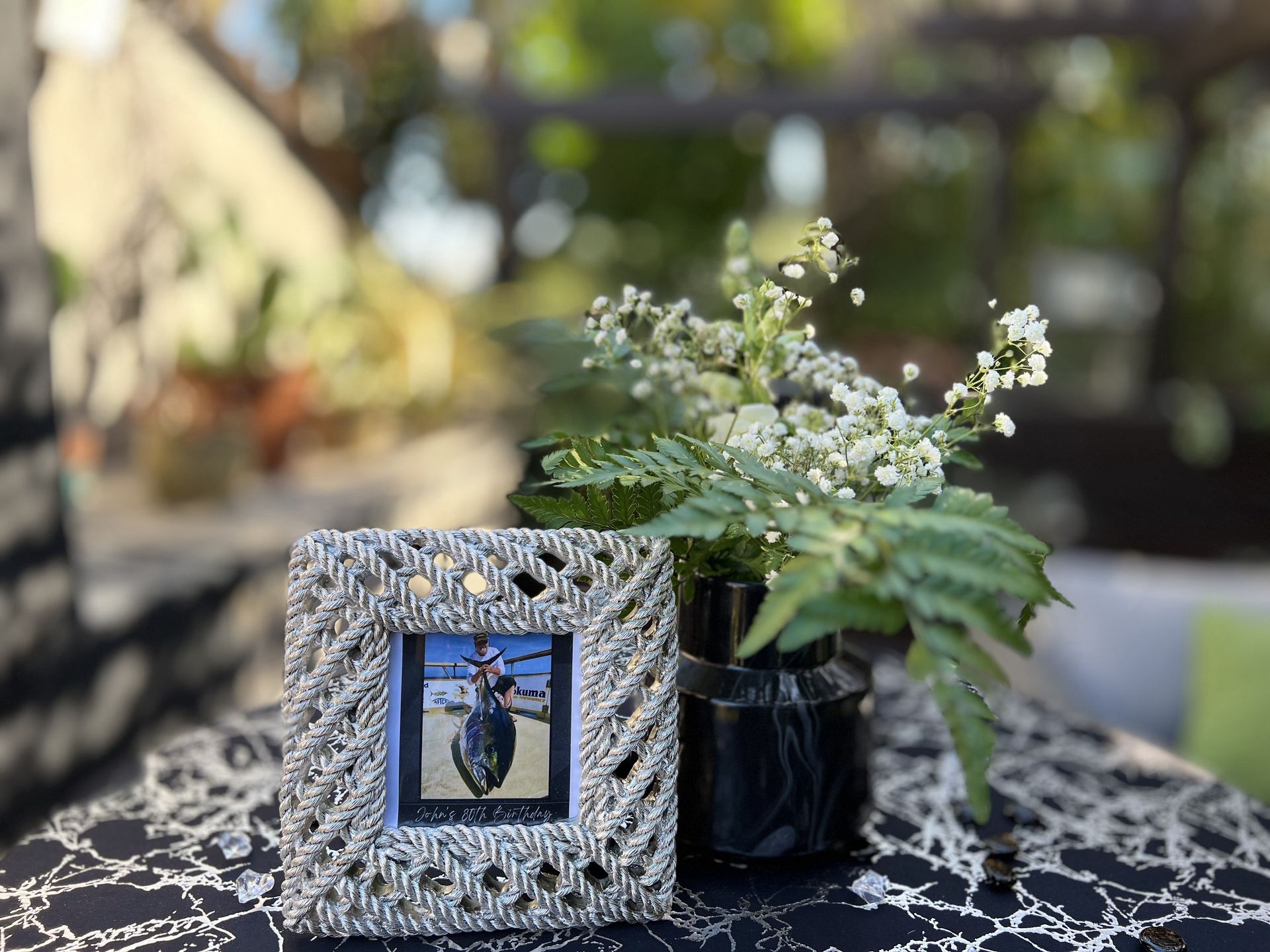 Picture frame and small flower arrangement on table. Outdoors, blurred background.