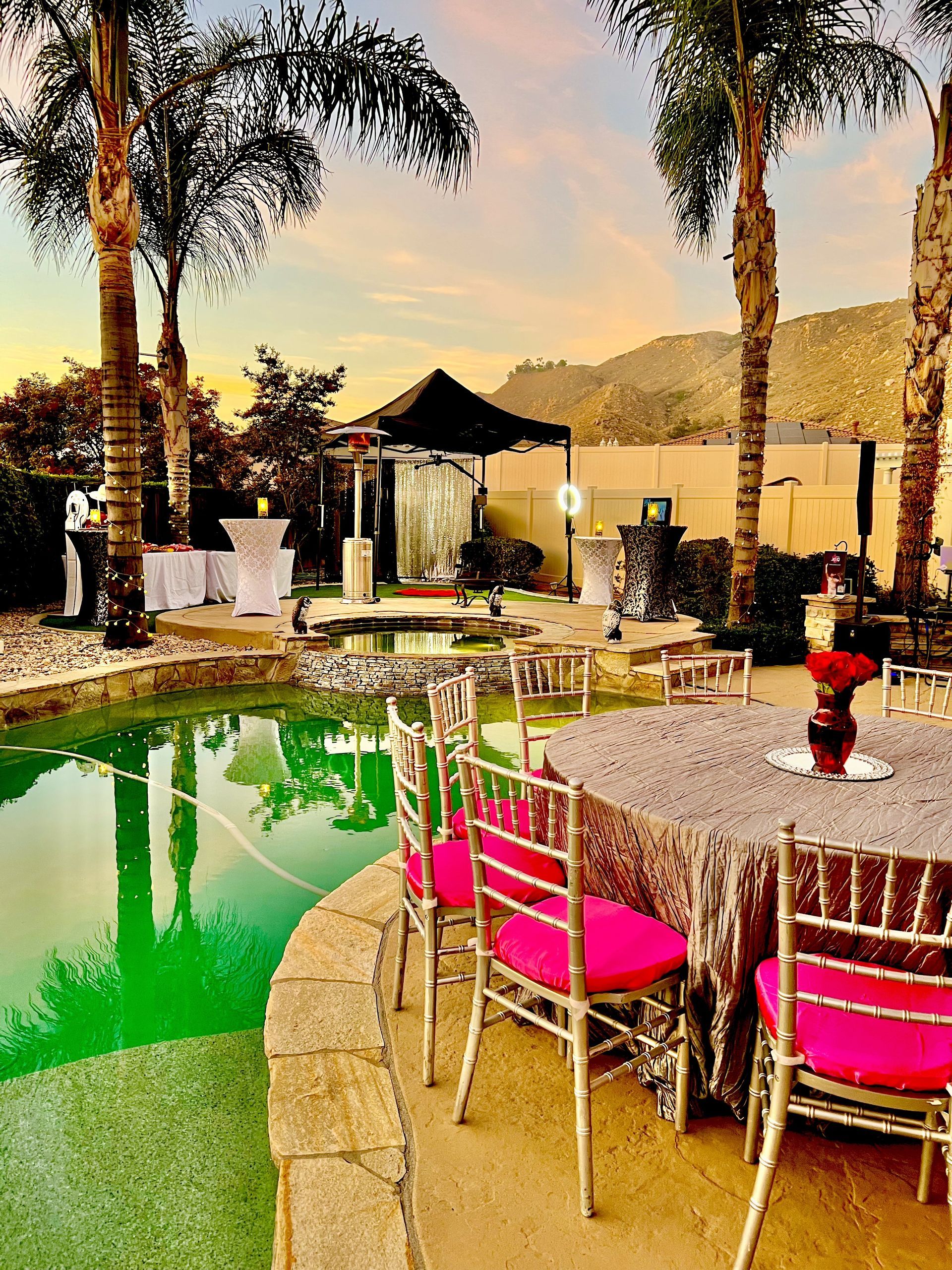 Outdoor event venue with tables, pool, palm trees, and gazebo at sunset.