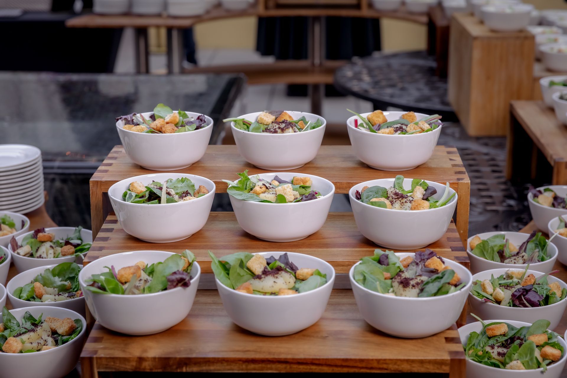 Salads in white bowls arranged on wooden tiered stands.
