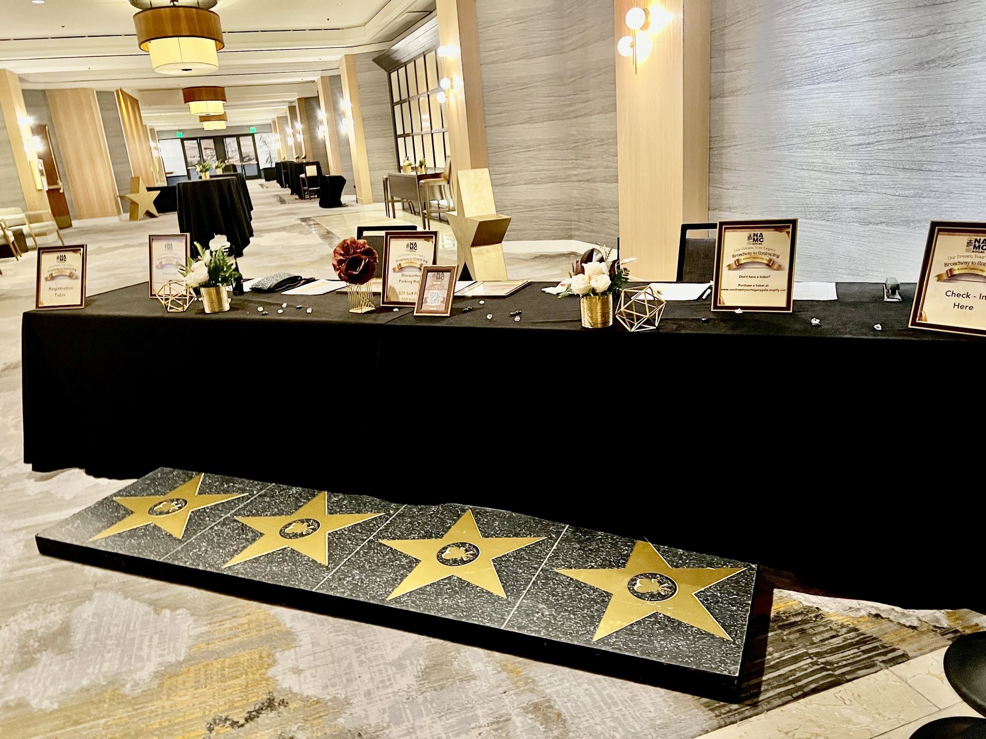 Event table with Hollywood Walk of Fame stars in front. Black tablecloth with awards, flowers.