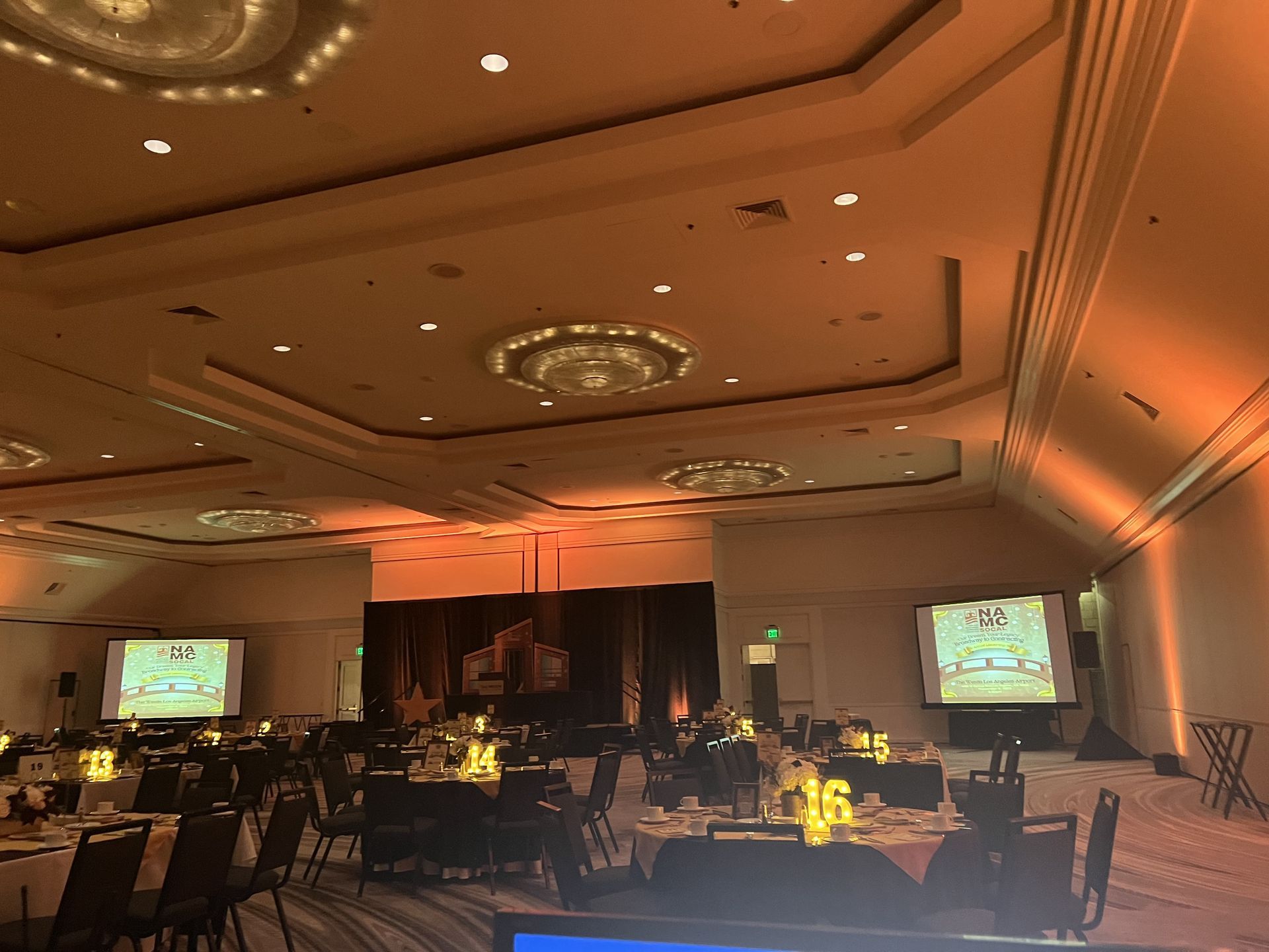 Banquet hall with tables, screens displaying content, and warm lighting.