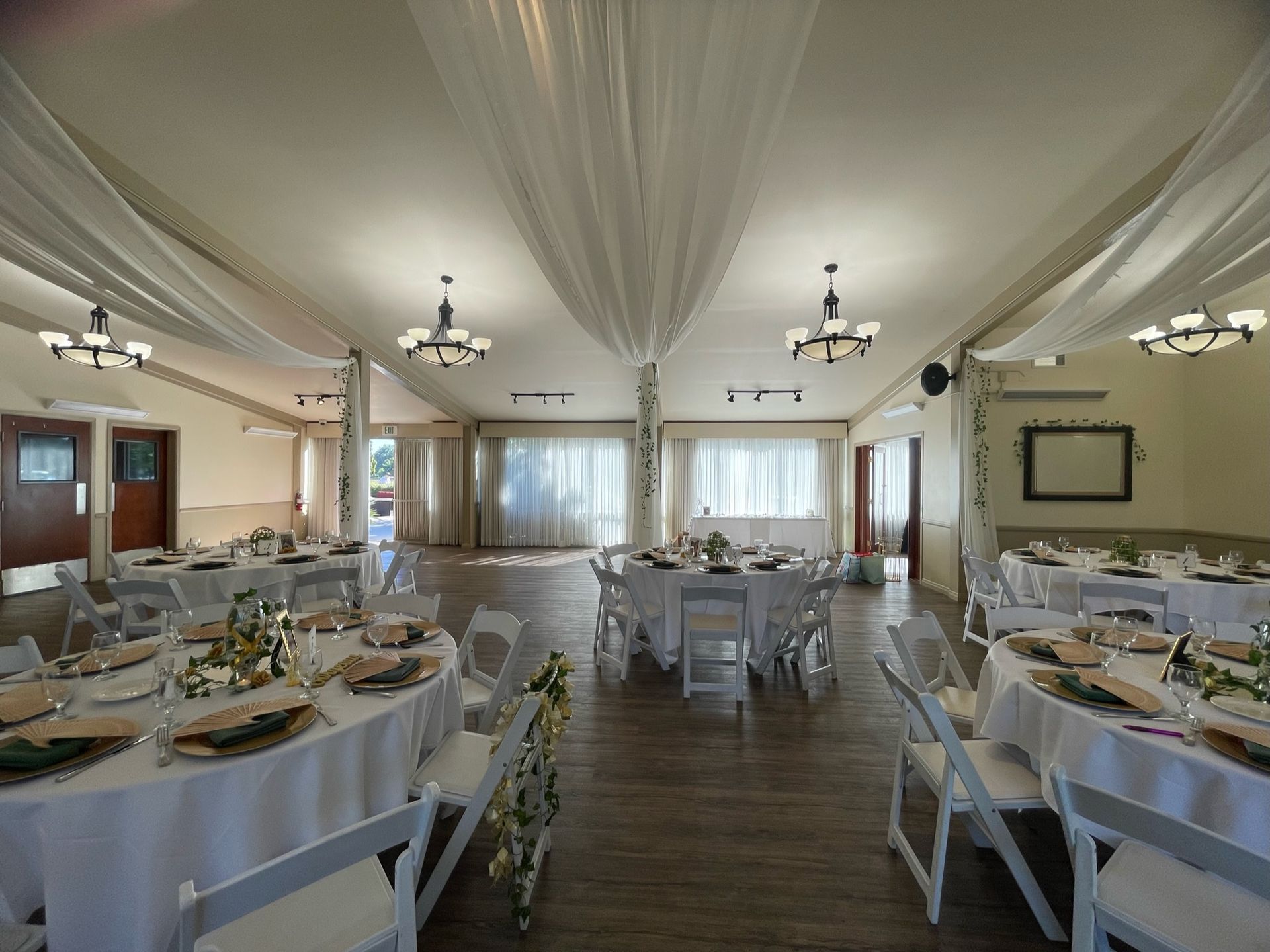Elegant banquet hall set up for a wedding, white draped ceiling and tables, windows, and chairs.