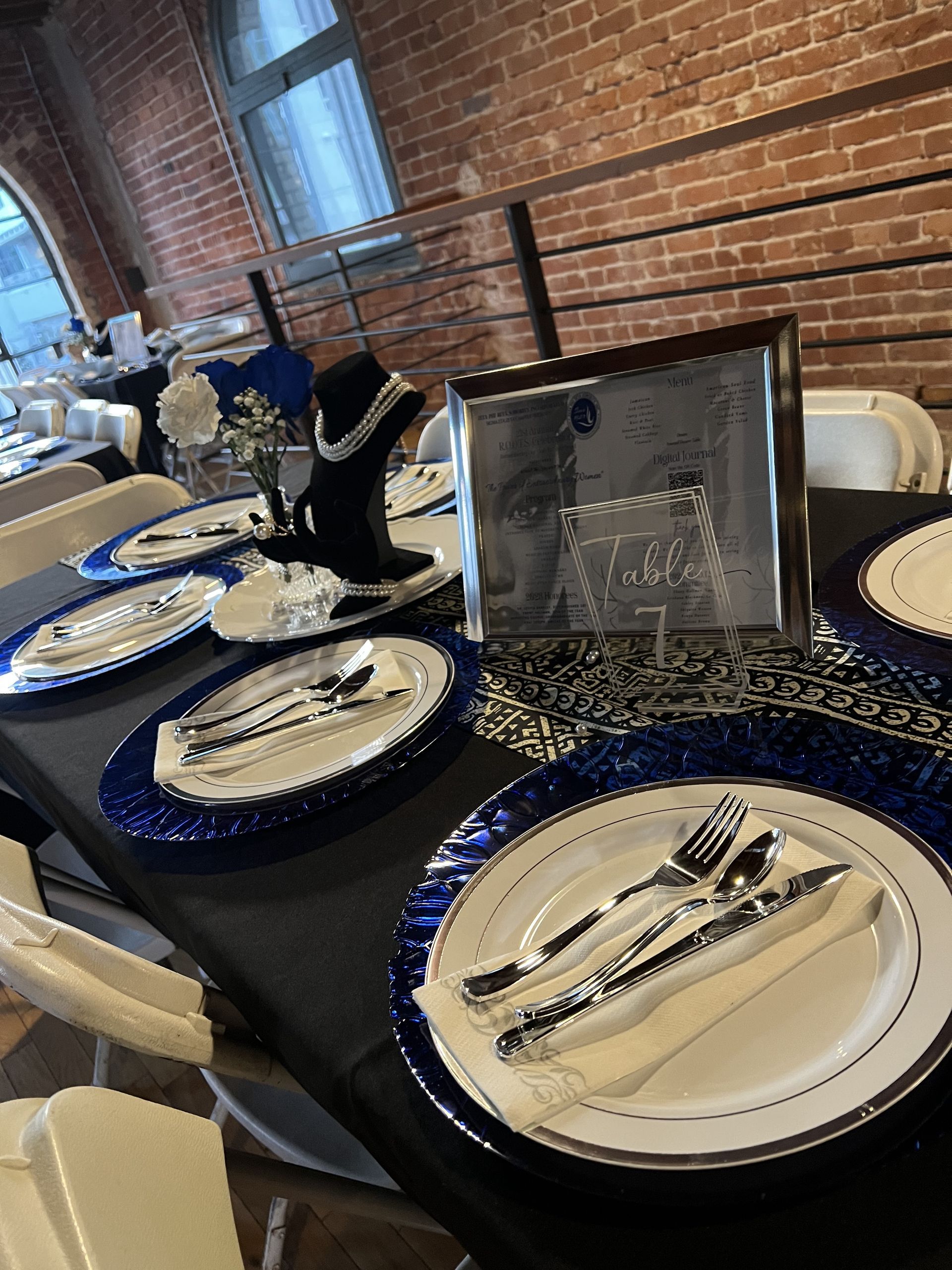 Table setting with blue and silver accents at an event with brick walls.