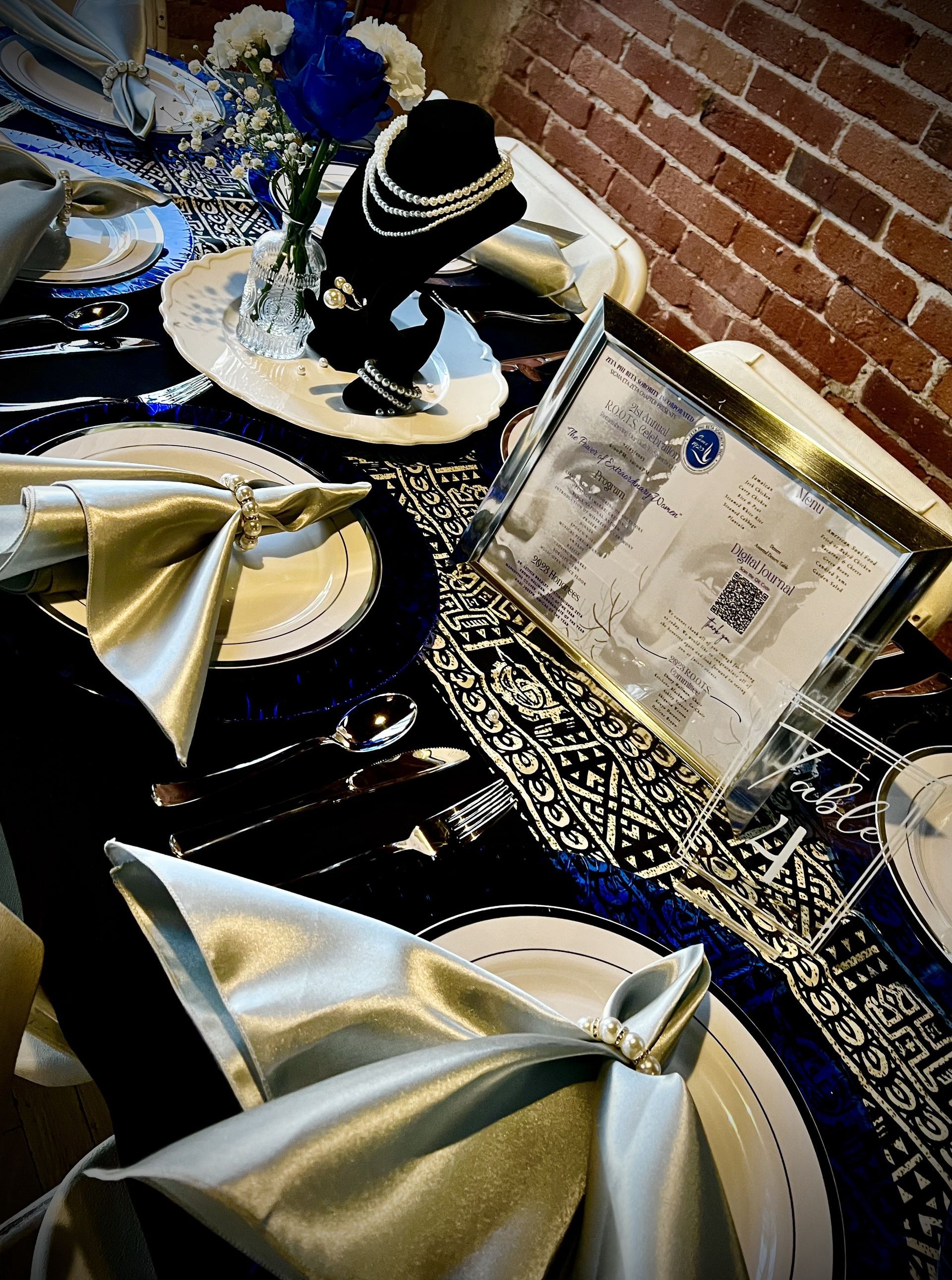 Elegant table setting with blue and silver accents, jewelry display, framed photograph, against a brick wall.