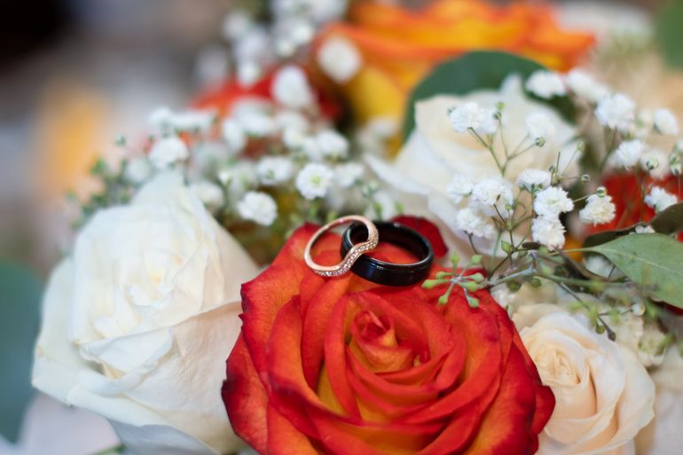 Wedding rings on an orange rose, surrounded by white and yellow flowers, greenery.