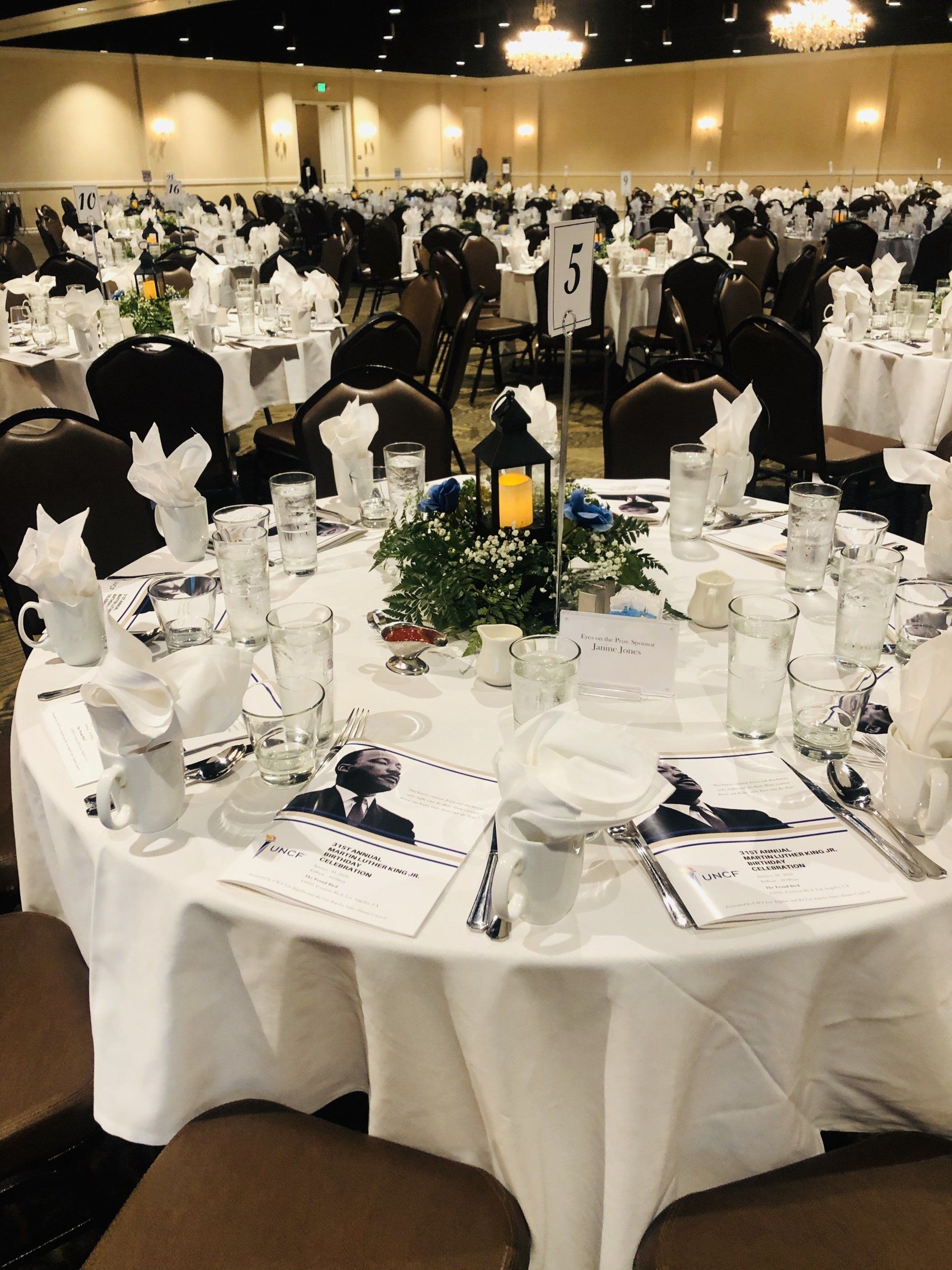 Round tables set for a banquet in a large hall with centerpieces, place settings, and chairs.