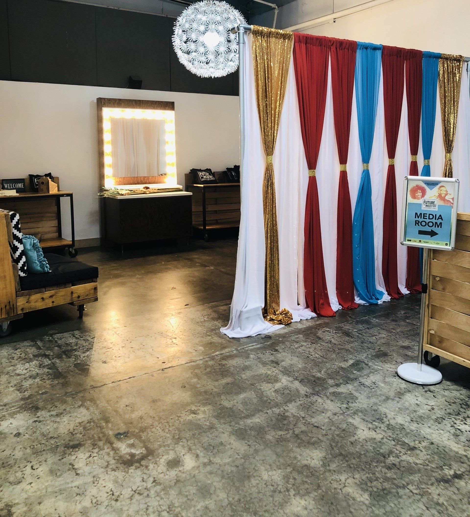 Event space with a photo booth; red, white, blue, and gold draped backdrop; a vanity mirror; and seating.