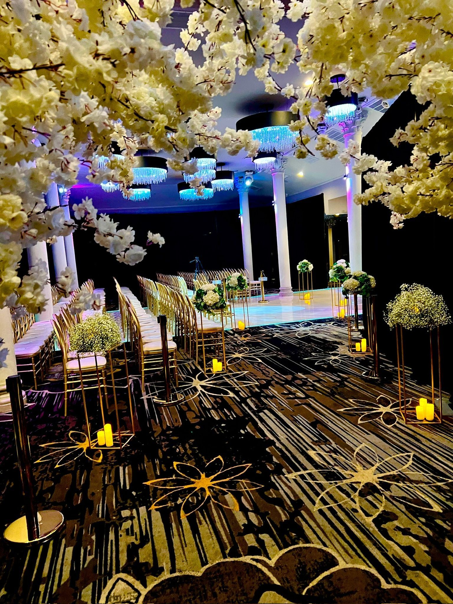 Wedding venue with floral arch, aisle with seating, and elevated stage, with golden and white decor.