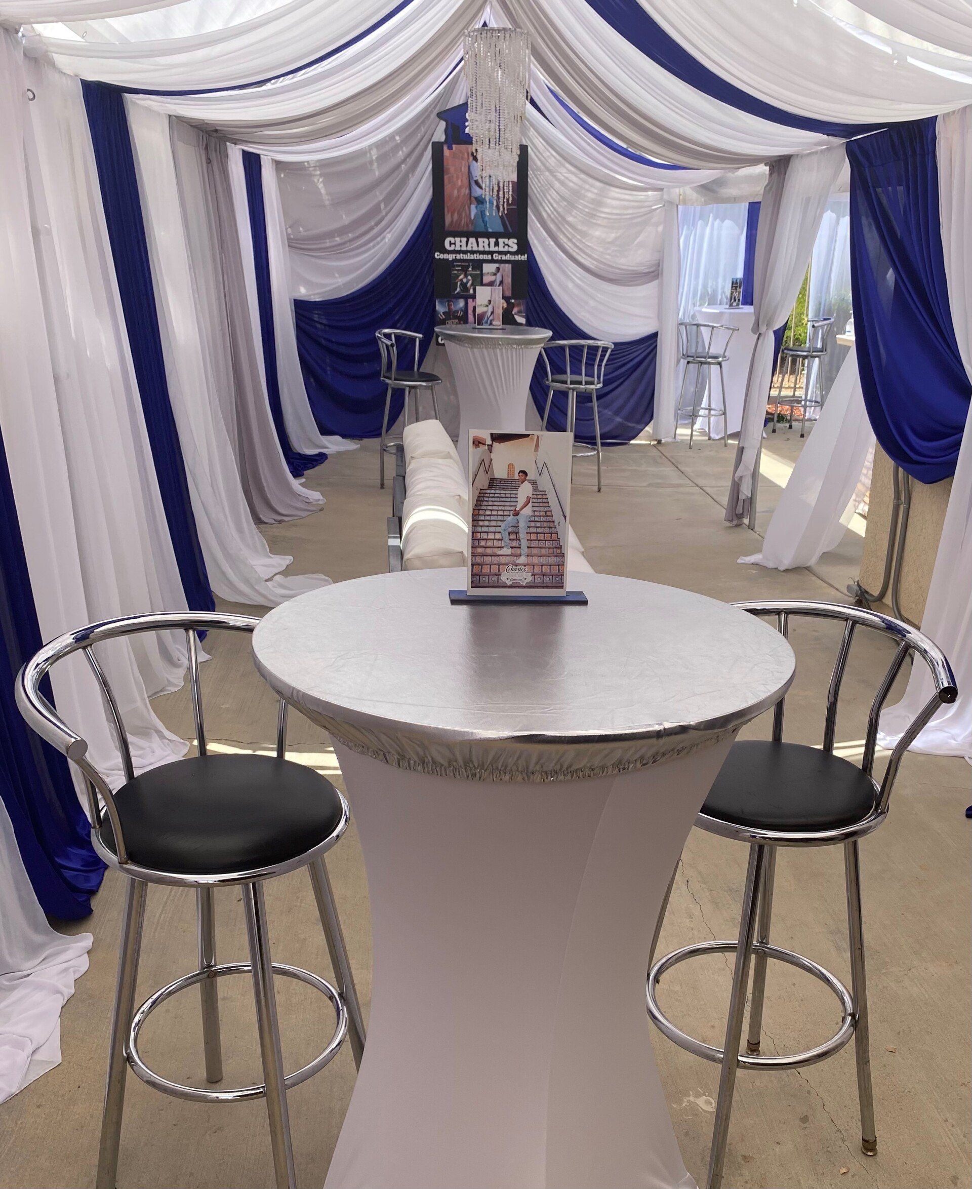 Small party setup with blue and white draped fabric, high-top table, and chrome bar stools.