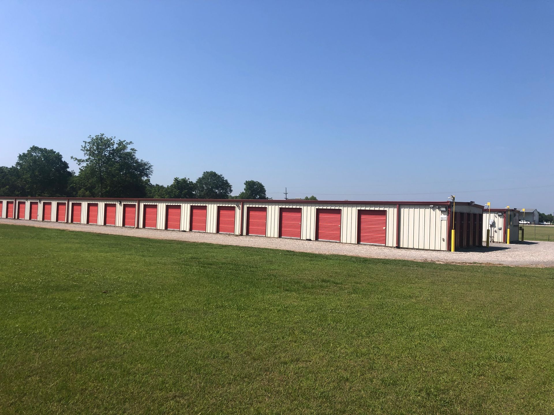 Storage units with red doors in a grassy field under a blue sky.