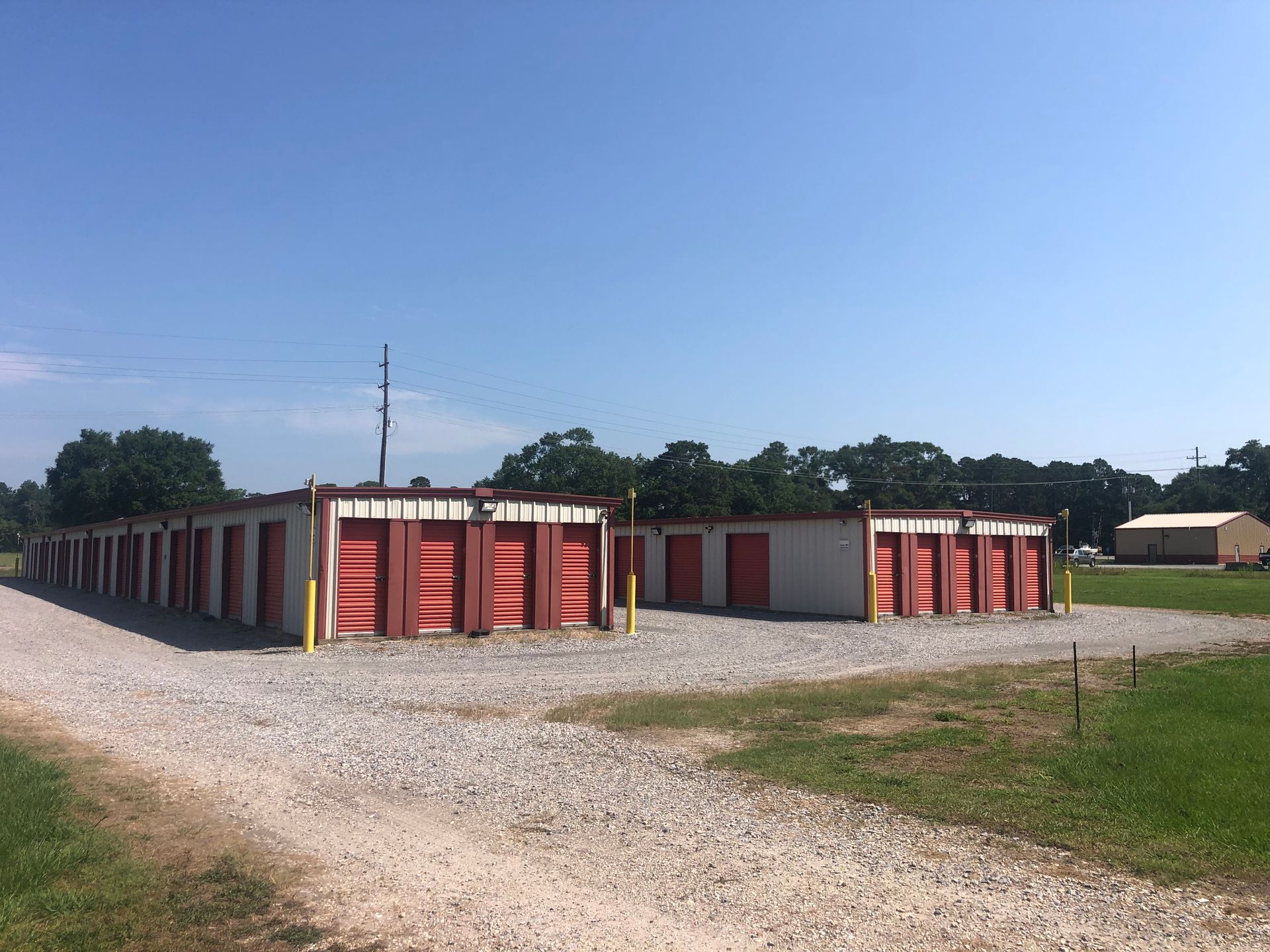 Storage units, red doors, gravel drive, green grass, sunny day.