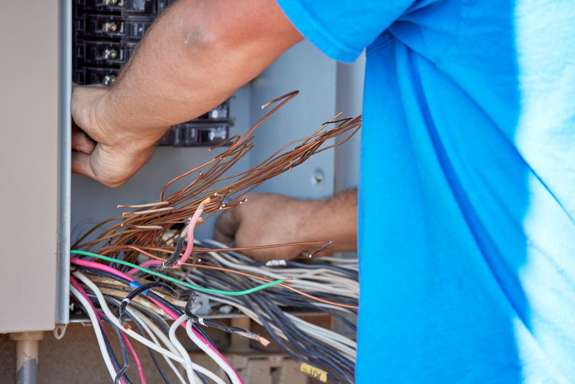 A man in a blue shirt is working on an electrical box.