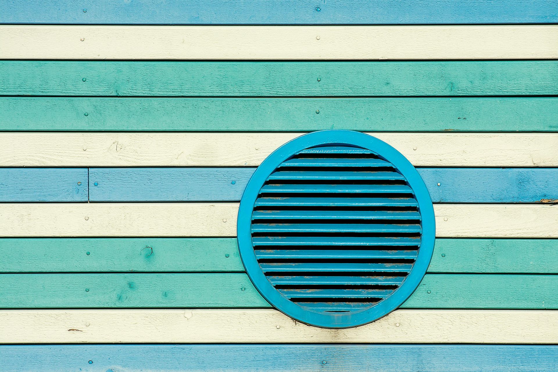 Blue circular vent on a turquoise and cream striped wall