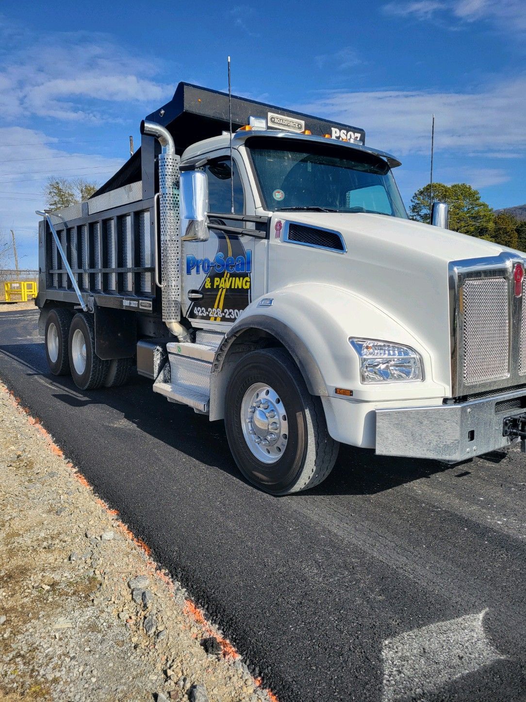 White dump truck on freshly paved asphalt road.