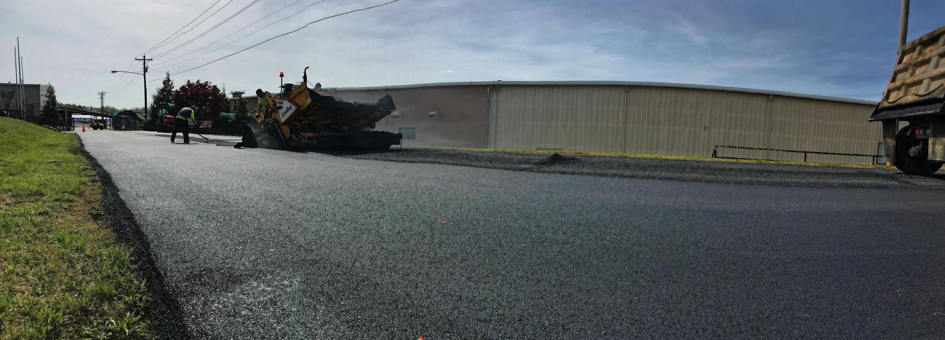 Road paving with a machine, a building in the background. Fresh asphalt on a sunny day.