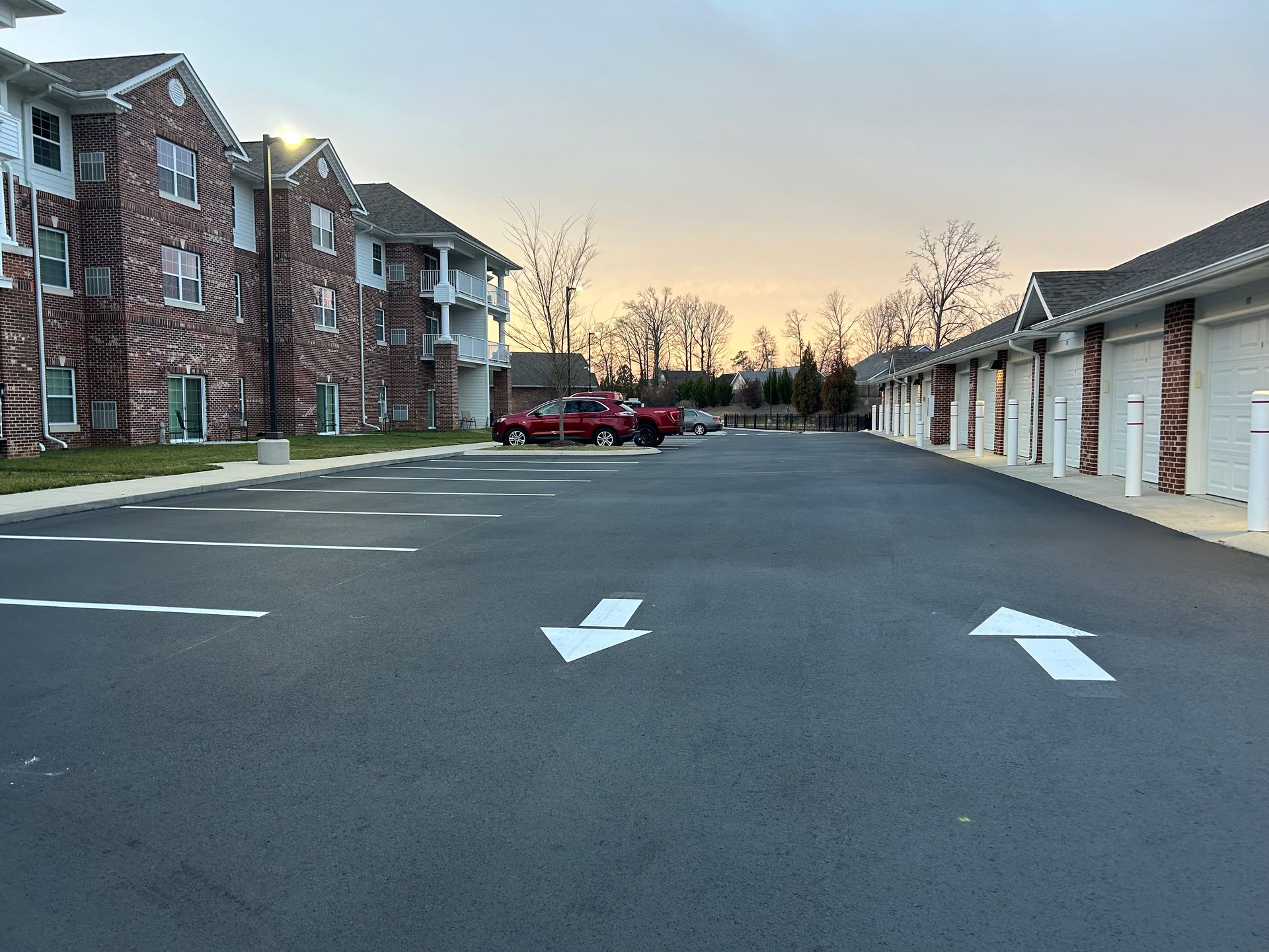 A parking lot with arrows and a brick apartment building and garages. Red truck is parked.