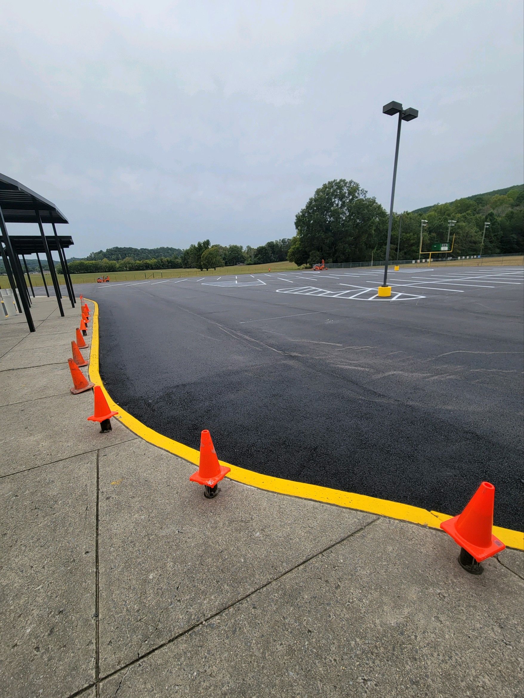 Orange traffic cones line the edge of a newly paved asphalt surface with yellow striping; outdoor setting.