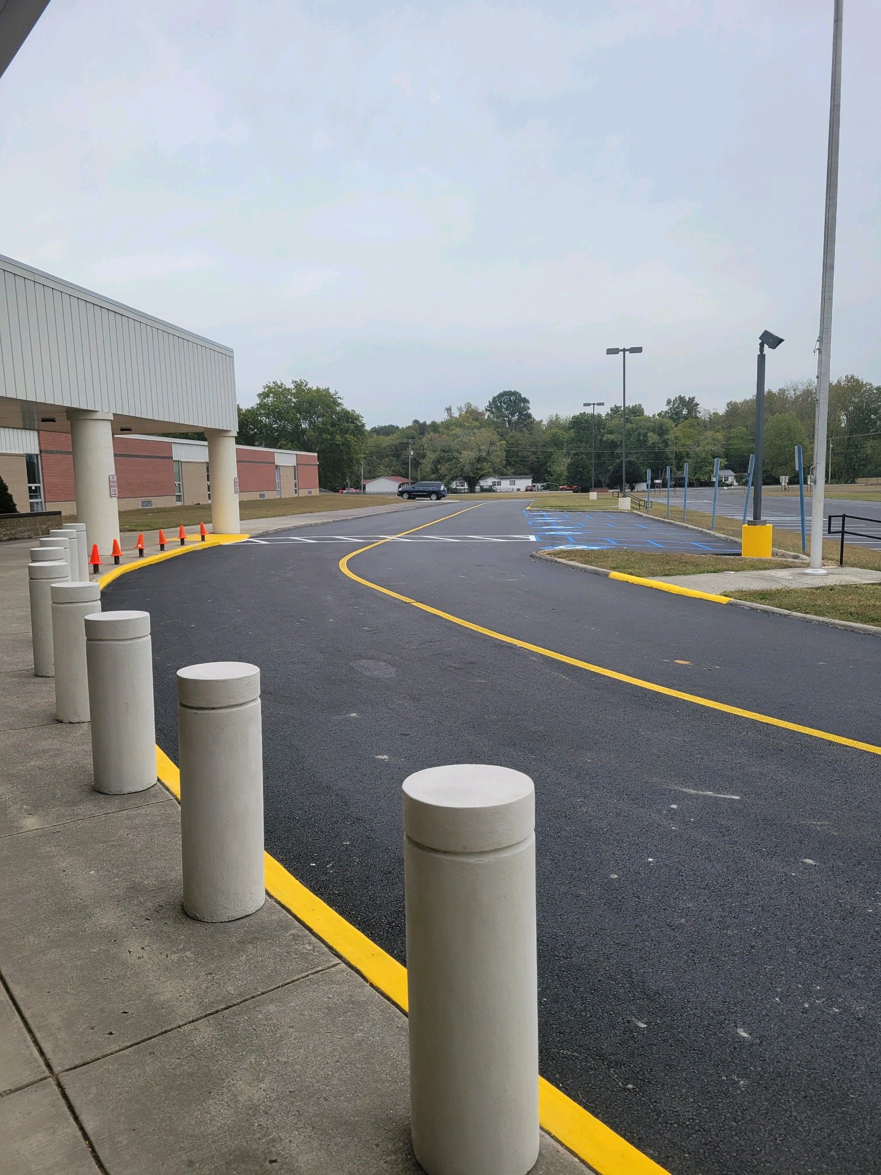 Entrance to a building with a newly paved road marked with yellow lines and concrete bollards.