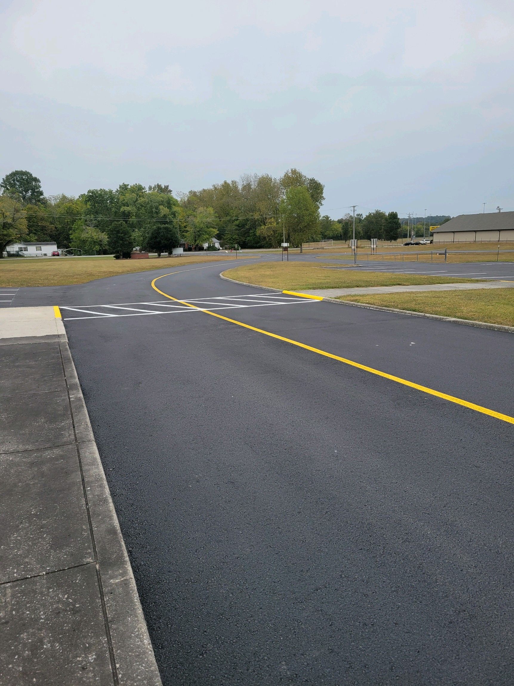 Paved road with yellow markings, curving through grassy area under cloudy sky.